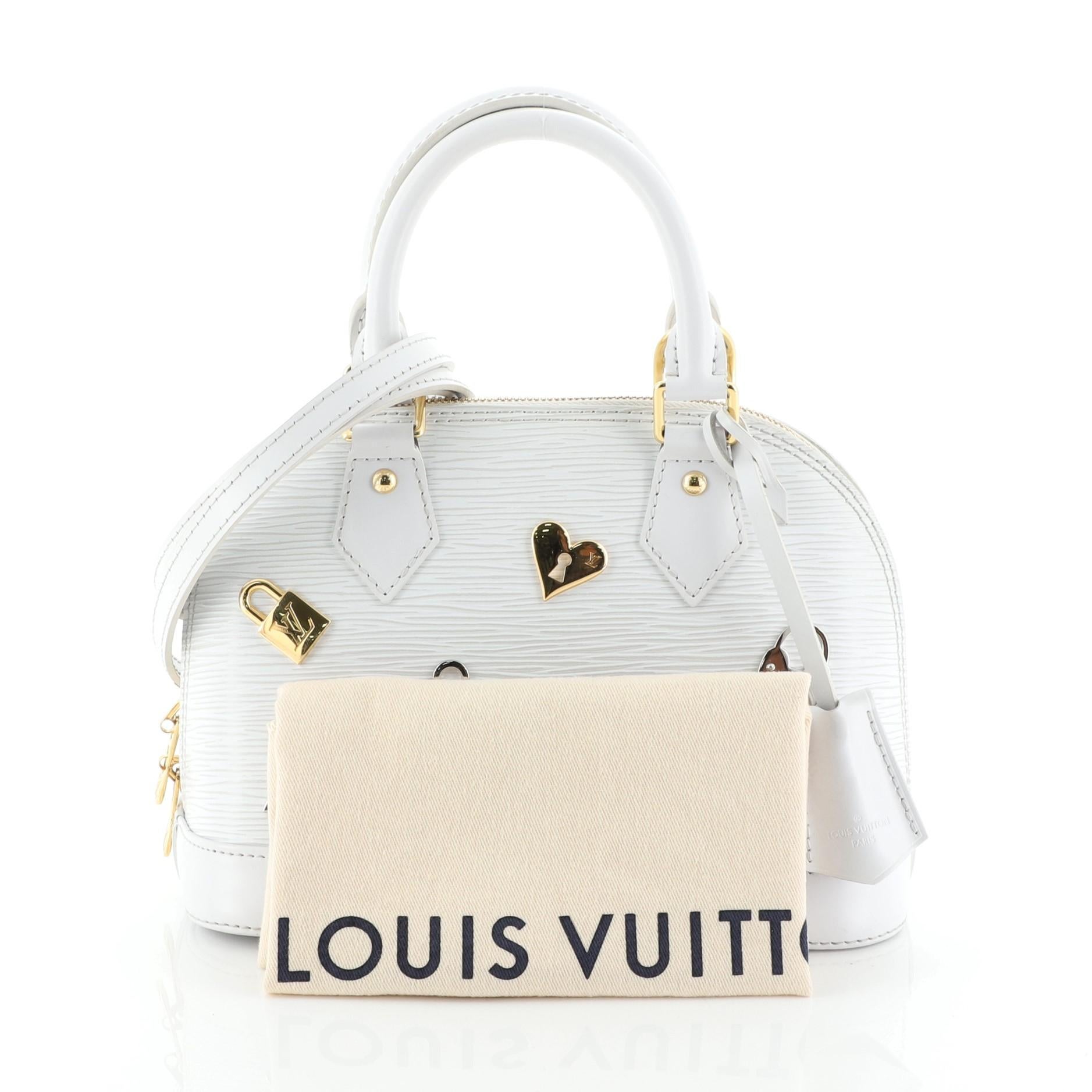 This Louis Vuitton Alma Handbag Love Lock Epi Leather BB, crafted in white epi leather, features dual rolled leather handles and gold and silver-tone hardware. Its all-around zip closure opens to a gray microfiber interior with slip pocket.