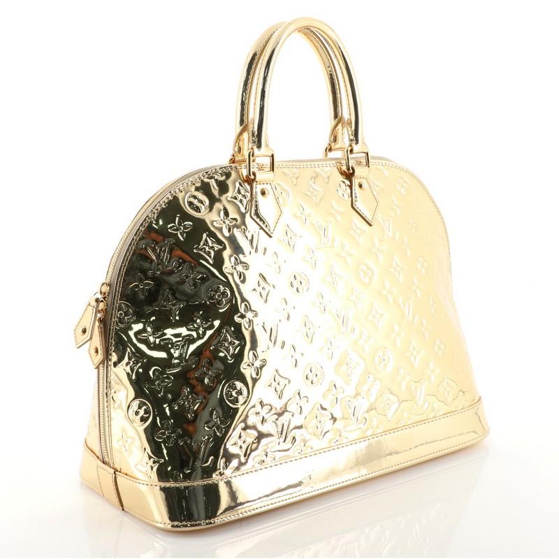 This Louis Vuitton Alma Handbag Miroir PVC GM, crafted from gold miroir PVC, features dual rolled handles, protective base studs, and gold-tone hardware. Its zip closure opens to a gray fabric interior with slip pockets. Authenticity code reads: