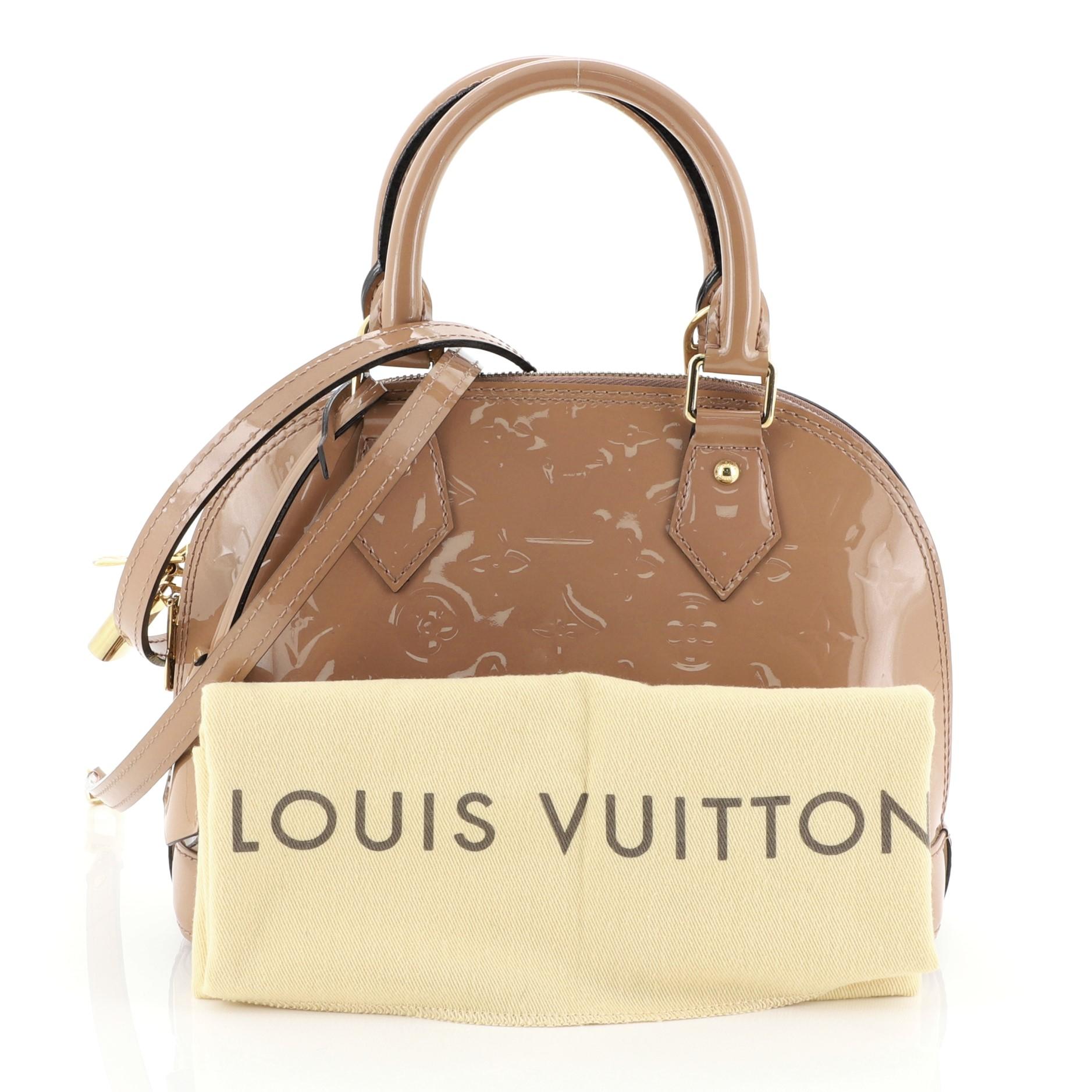 This Louis Vuitton Alma Handbag Monogram Vernis BB, crafted from neutral monogram vernis leather, features dual rolled handles, protective base studs, and gold-tone hardware. Its two-way zip closure opens to a neutral fabric interior with slip