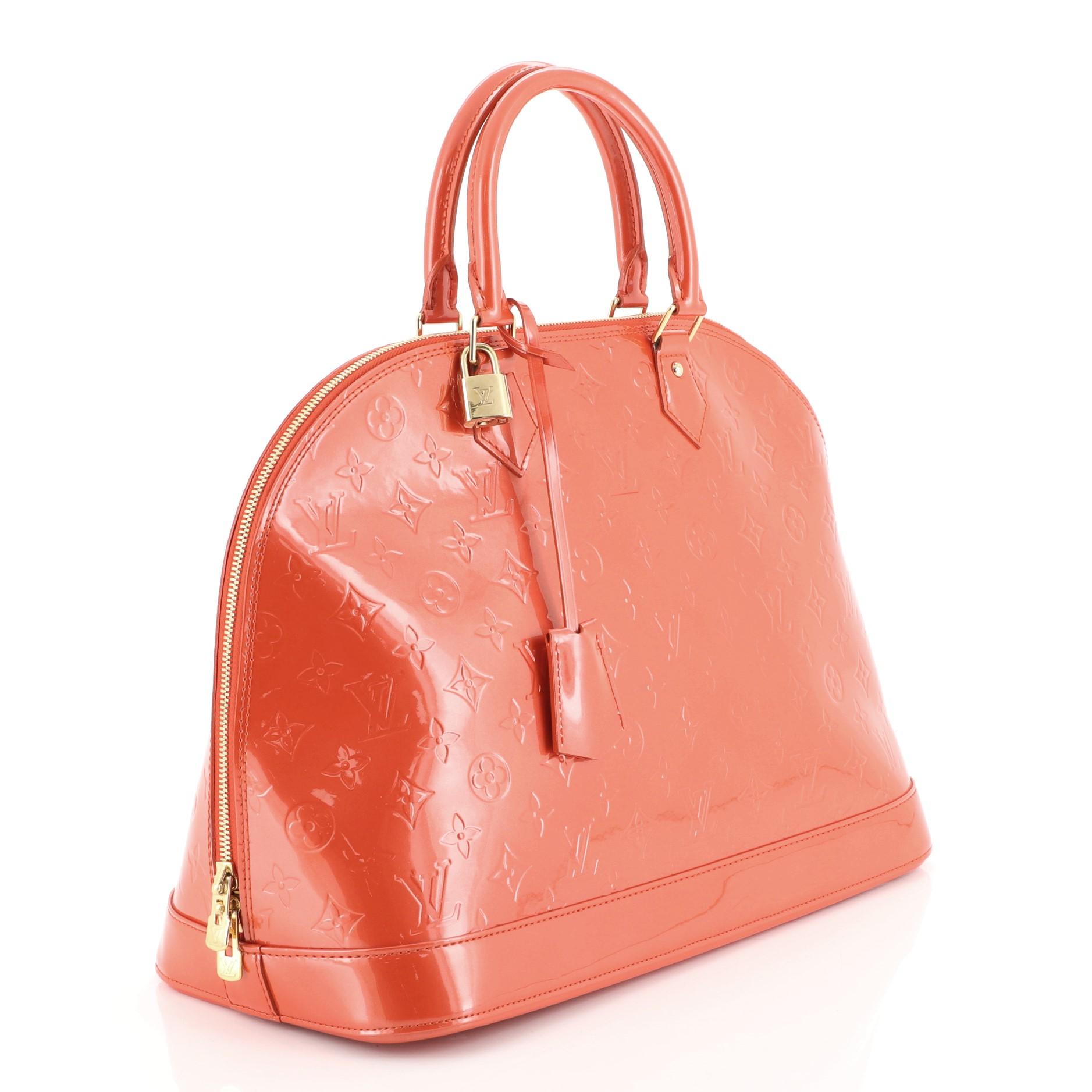 This Louis Vuitton Alma Handbag Monogram Vernis MM, crafted in orange monogram vernis leather, features dual rolled leather handles, protective base studs, and gold-tone hardware. Its zip closure opens to an orange fabric interior with slip pocket.
