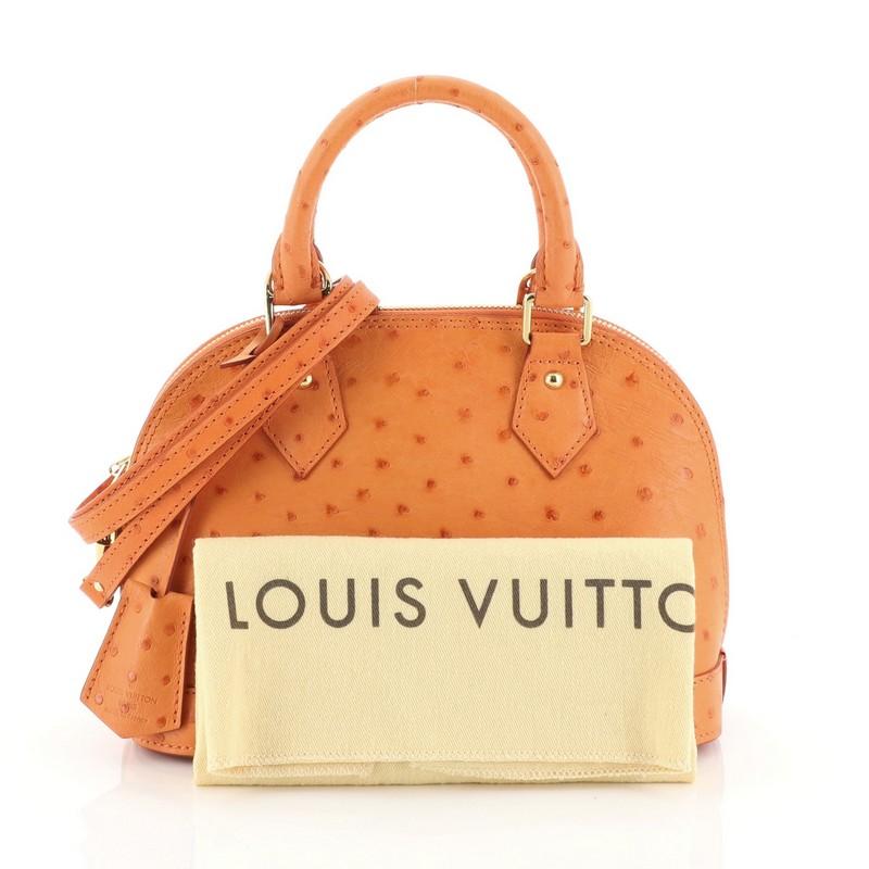 This Louis Vuitton Alma Handbag Ostrich BB, crafted in genuine orange ostrich skin, features a sturdy base, protective base studs, dual-rolled handles and gold-tone hardware. Its zip around closure opens to an orange leather interior with a side