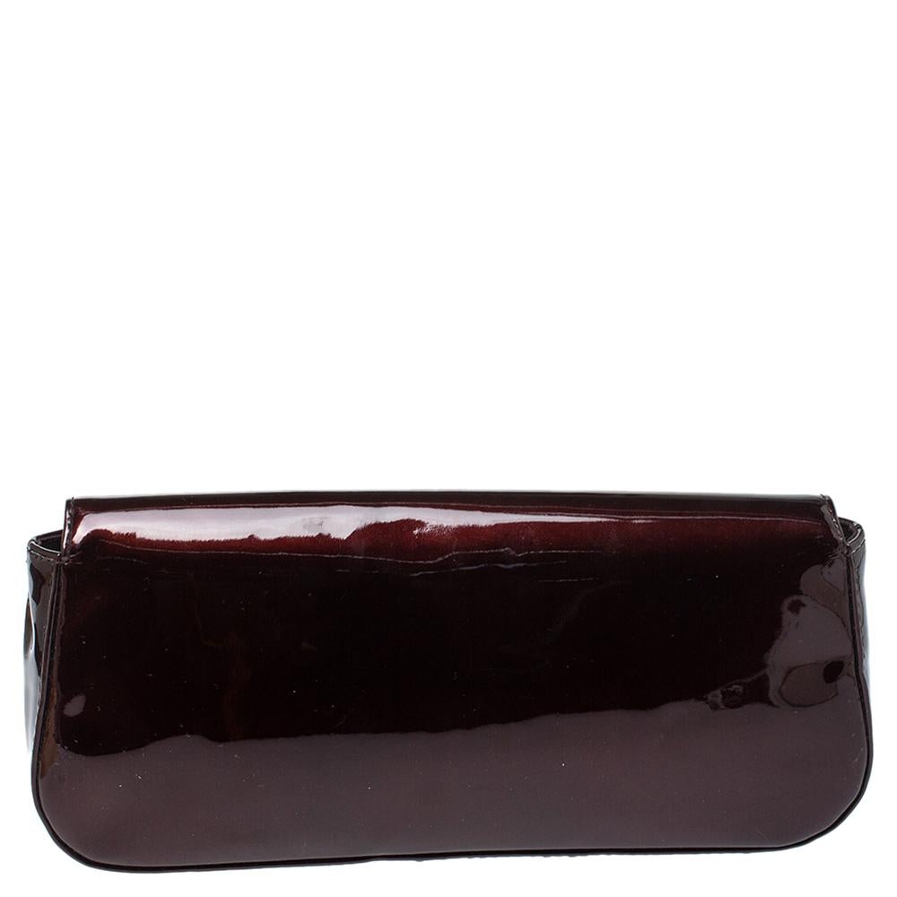 Well-crafted and overflowing with style, this Sobe clutch is from Louis Vuitton. It has a patent leather exterior, fabric interior, and an exaggerated LV adorned on the flap. This creation will lift all your evening gowns and elegant outfits