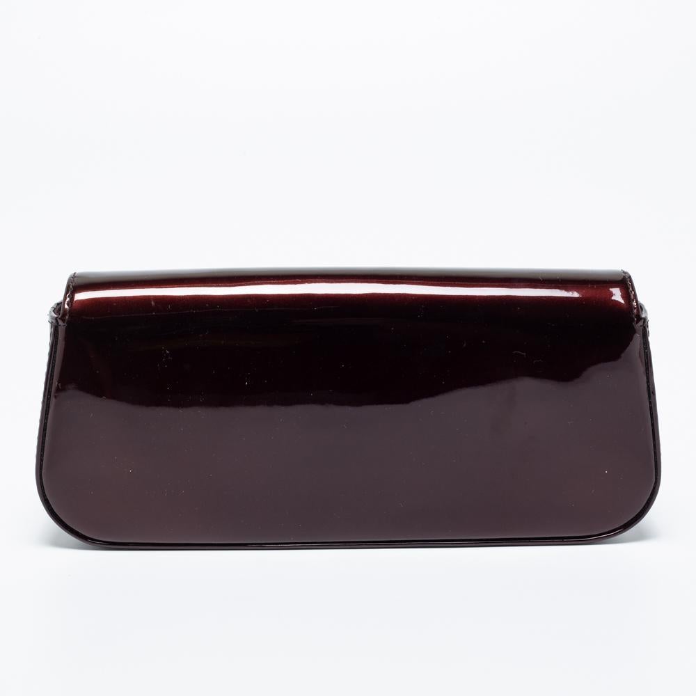 This Sobe clutch from the house of Louis Vuitton is perfect for dinner dates and evening outings. It is fashioned in a sleek silhouette with Monogram Vernis and detailed with a gold-tone 'LV' logo on the front. This clutch offers just the right