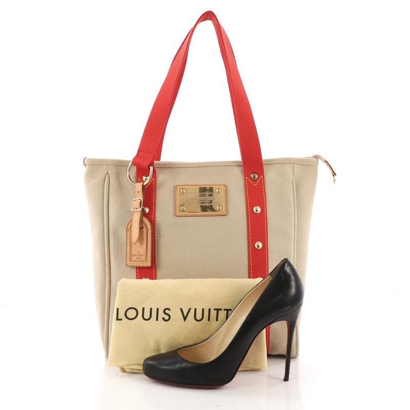 This Louis Vuitton Antigua Tote Canvas MM, crafted with beige canvas, features dual flat red canvas shoulder straps with stud detailing, 