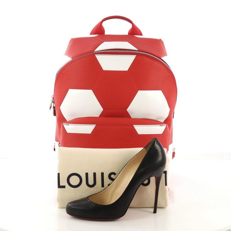 This Louis Vuitton Apollo Backpack Limited Edition FIFA World Cup Epi Leather, crafted from red epi leather, features a top handle, adjustable back straps, hexagonal pattern of footballs, exterior front zip pocket, and silver-tone hardware. Its zip