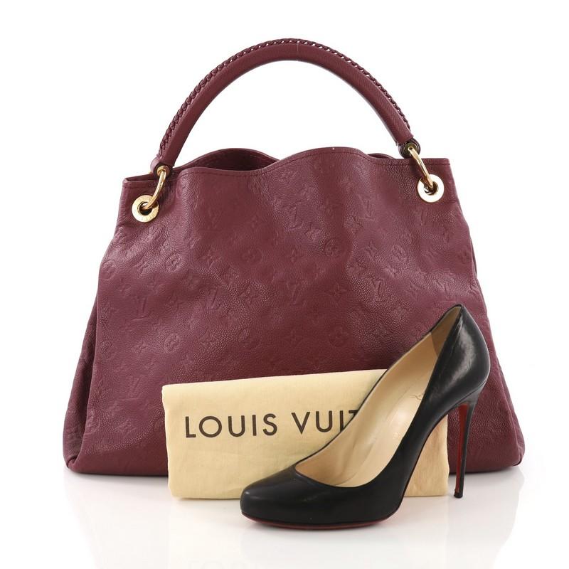 This Louis Vuitton Artsy Handbag Monogram Empreinte Leather MM, crafted from purple monogram embossed empreinte leather, features a single looped braided top handle, protective base studs, and gold-tone hardware. Its wide open top showcases a purple