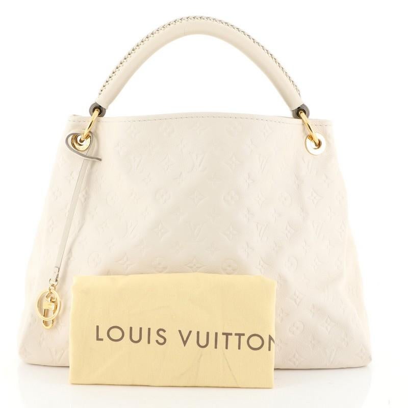 This Louis Vuitton Artsy Handbag Monogram Empreinte Leather MM, crafted from neutral monogram empreinte leather, features a single looped braided top handle, protective base studs, and gold-tone hardware. Its wide open top showcases a white fabric