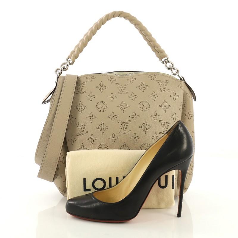 This Louis Vuitton Babylone Handbag Mahina Leather BB, crafted from taupe mahina monogram perforated leather, features leather covered chain strap, protective base studs and silver-tone hardware. Its zip closure opens to a brown microfiber interior