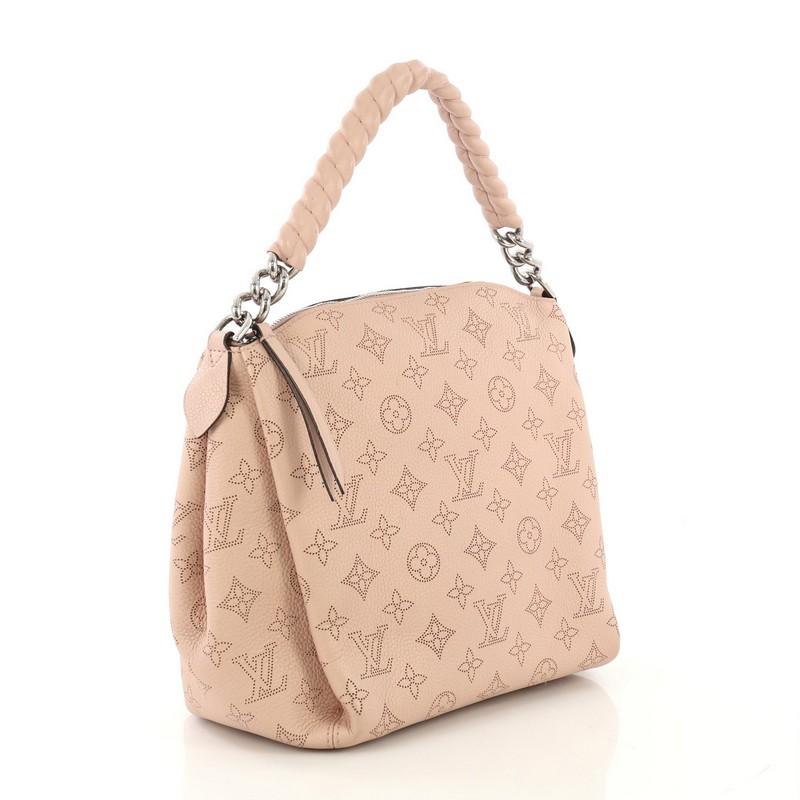 This Louis Vuitton Babylone Handbag Mahina Leather BB, crafted from pink mahina monogram perforated leather, features leather covered chain strap, protective base studs, and silver-tone hardware. Its zip closure opens to a dark brown microfiber
