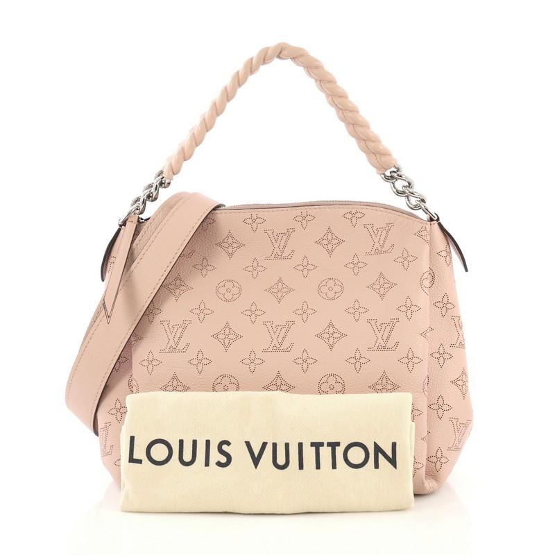 This Louis Vuitton Babylone Handbag Mahina Leather BB, crafted from pink mahina monogram perforated leather, features leather covered chain strap, protective base studs and silver-tone hardware. Its zip closure opens to a dark brown microfiber