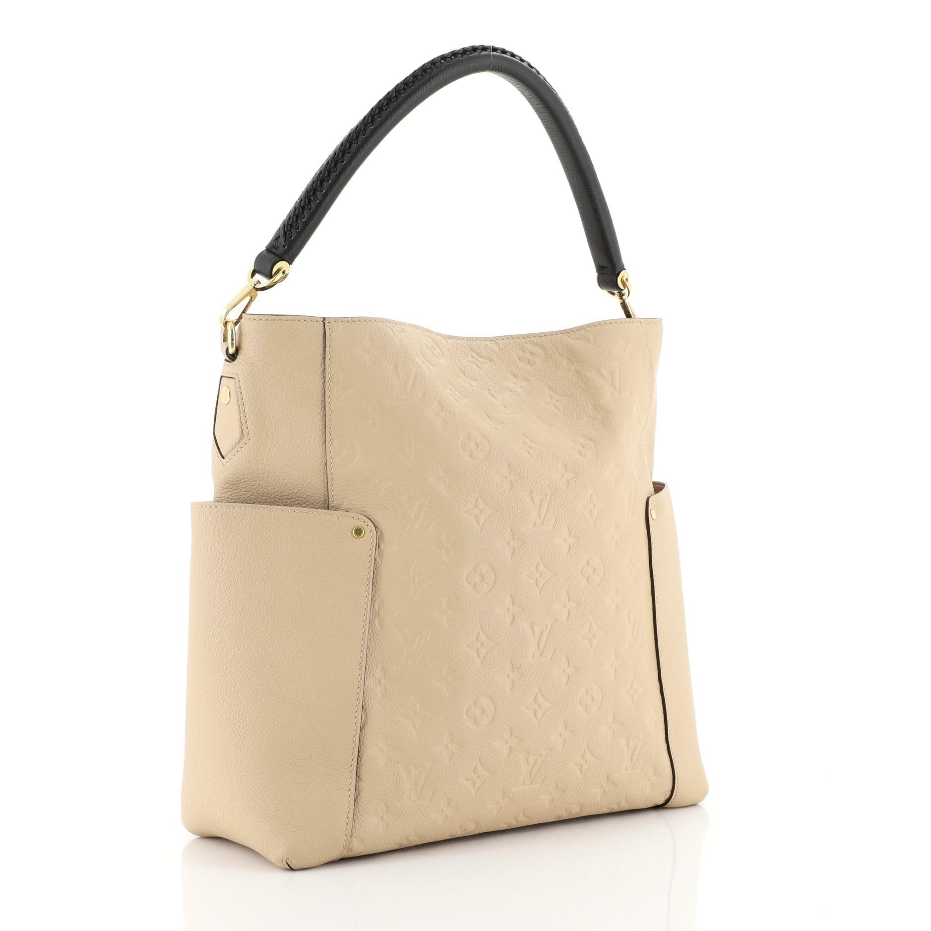 This Louis Vuitton Bagatelle Hobo Monogram Empreinte Leather, crafted from neutral monogram empreinte leather, features a braided handle, exterior flat pocket on each side, and gold-tone hardware. Its wide open top showcases a neutral fabric