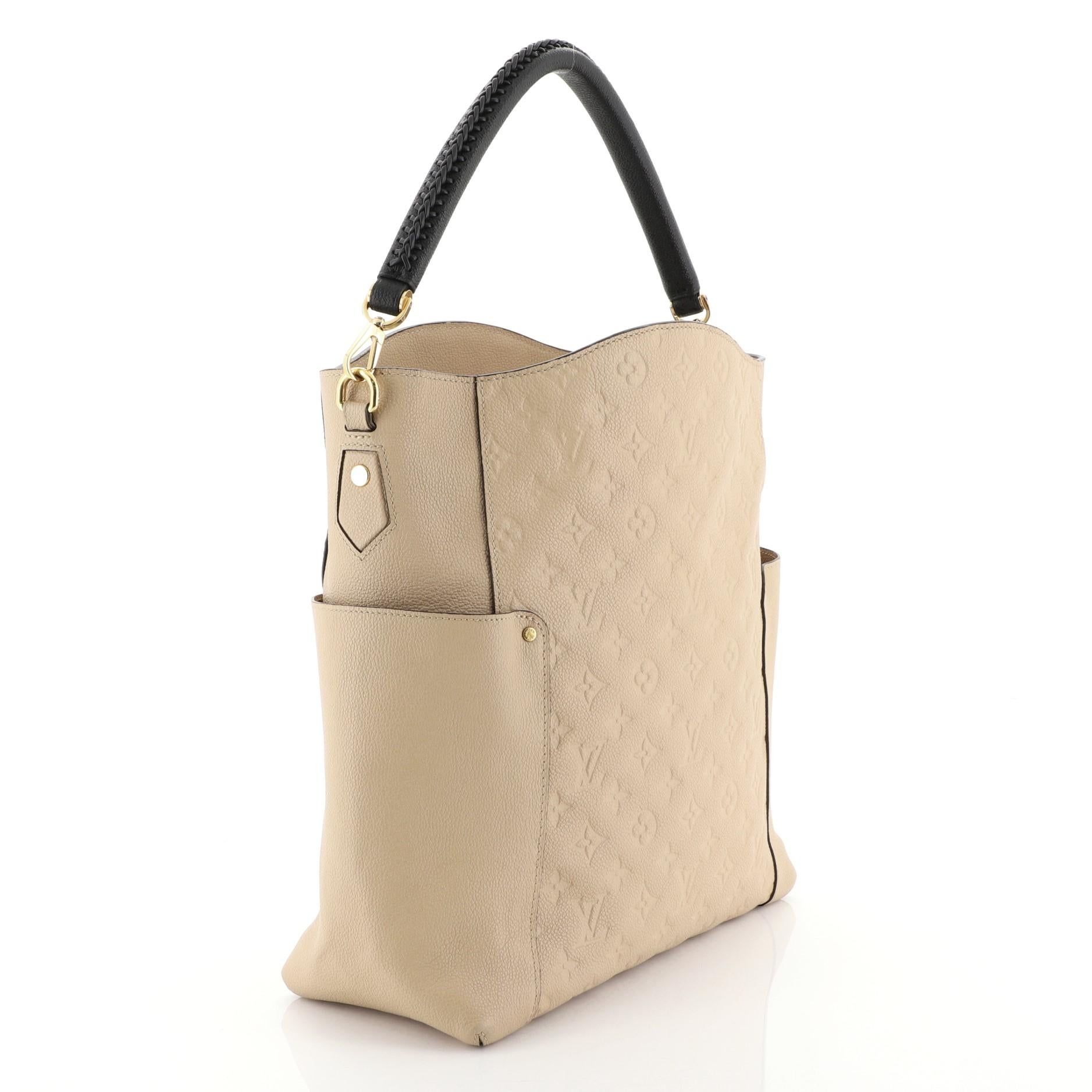 This Louis Vuitton Bagatelle Hobo Monogram Empreinte Leather, crafted from neutral monogram empreinte leather, features a braided handle, exterior flat pockets on each side, and gold-tone hardware. Its wide open top showcases a neutral fabric