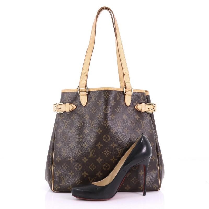 This Louis Vuitton Batignolles Handbag Monogram Canvas Vertical, crafted in brown monogram coated canvas, features cowhide leather trim and handles, side belt strap details, and gold-tone hardware. Its wide open top showcases a brown fabric interior
