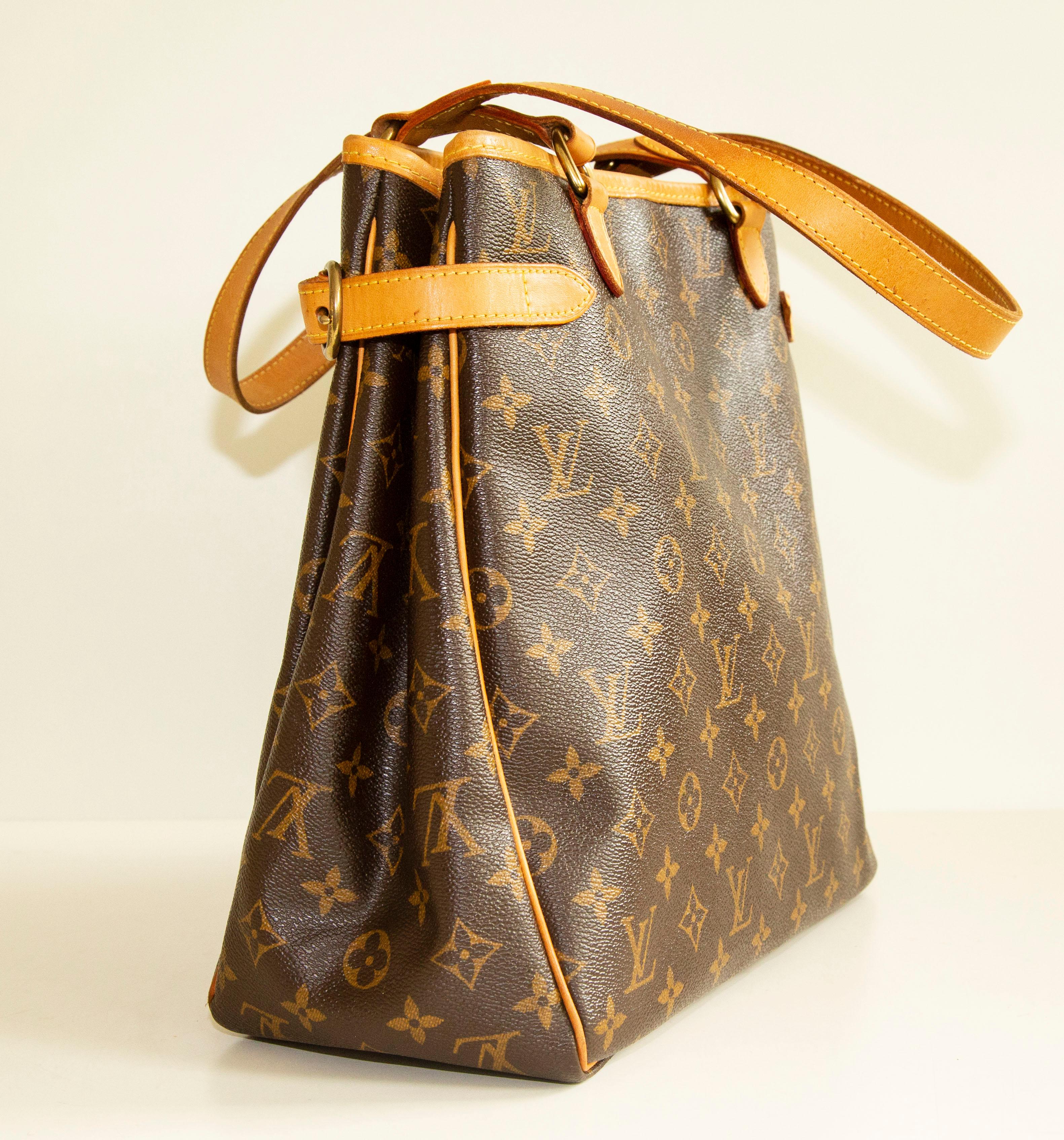 An authentic Louis Vuitton Batignolles vertical shoulder bag. The bag features an LV monogram canvas, Vachetta leather trim, and gold-toned hardware. The interior is lined with brown fabric and there are two side pockets, one slip pocket and one