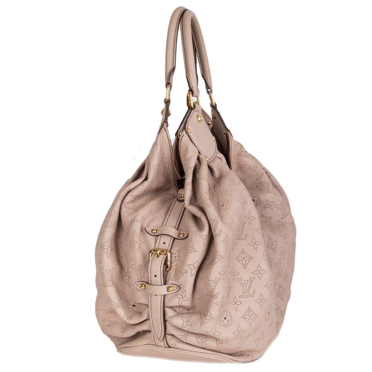 Louis Vuitton 'Mahina GM' hobo bag in sand beige perforated monogram leather and it features two handles and gold-tone hardware. The push-lock opens to a spacious beige alcantara lined interior with one zipper pocket against the back and a D ring.