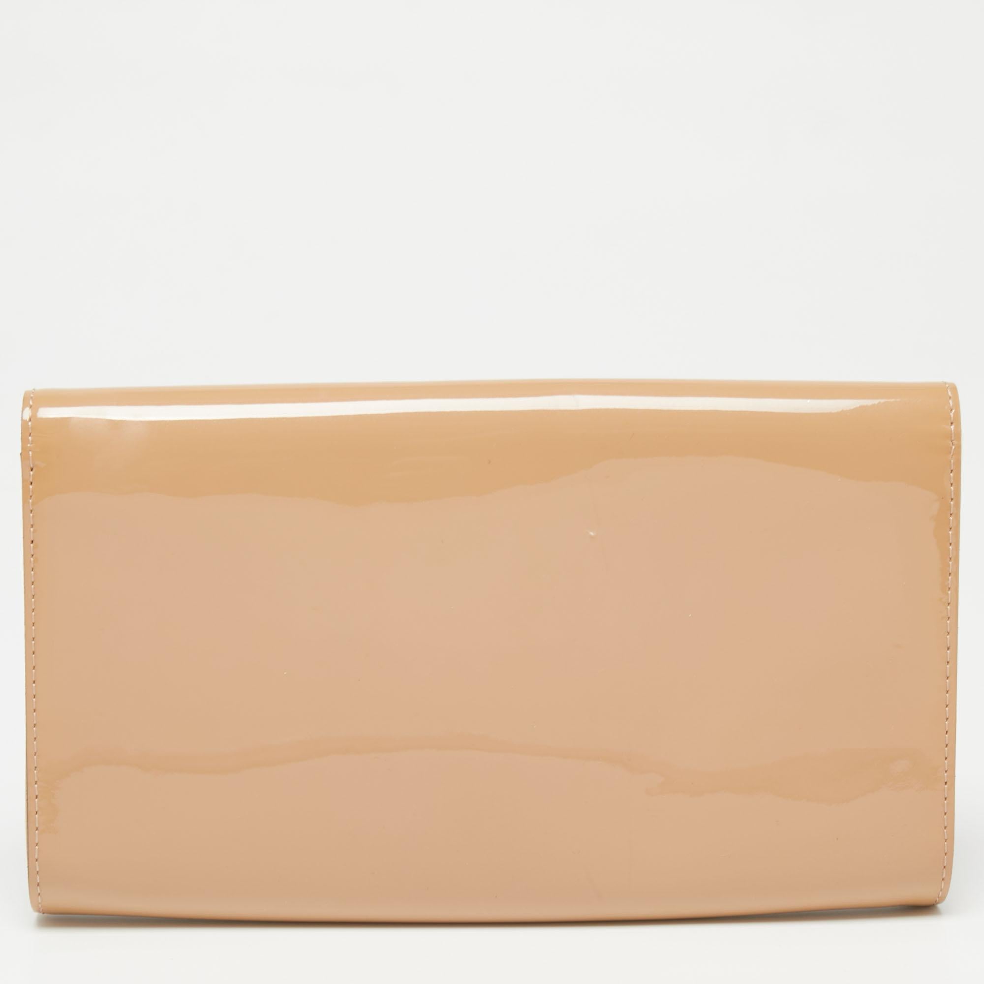 This beige Louise clutch by Louis Vuitton is well-crafted and overflowing with style. It has a glossy patent leather exterior, a fabric interior, and a large gold-tone 'LV' adorned on the flap. From the way it has been crafted to the way it has been