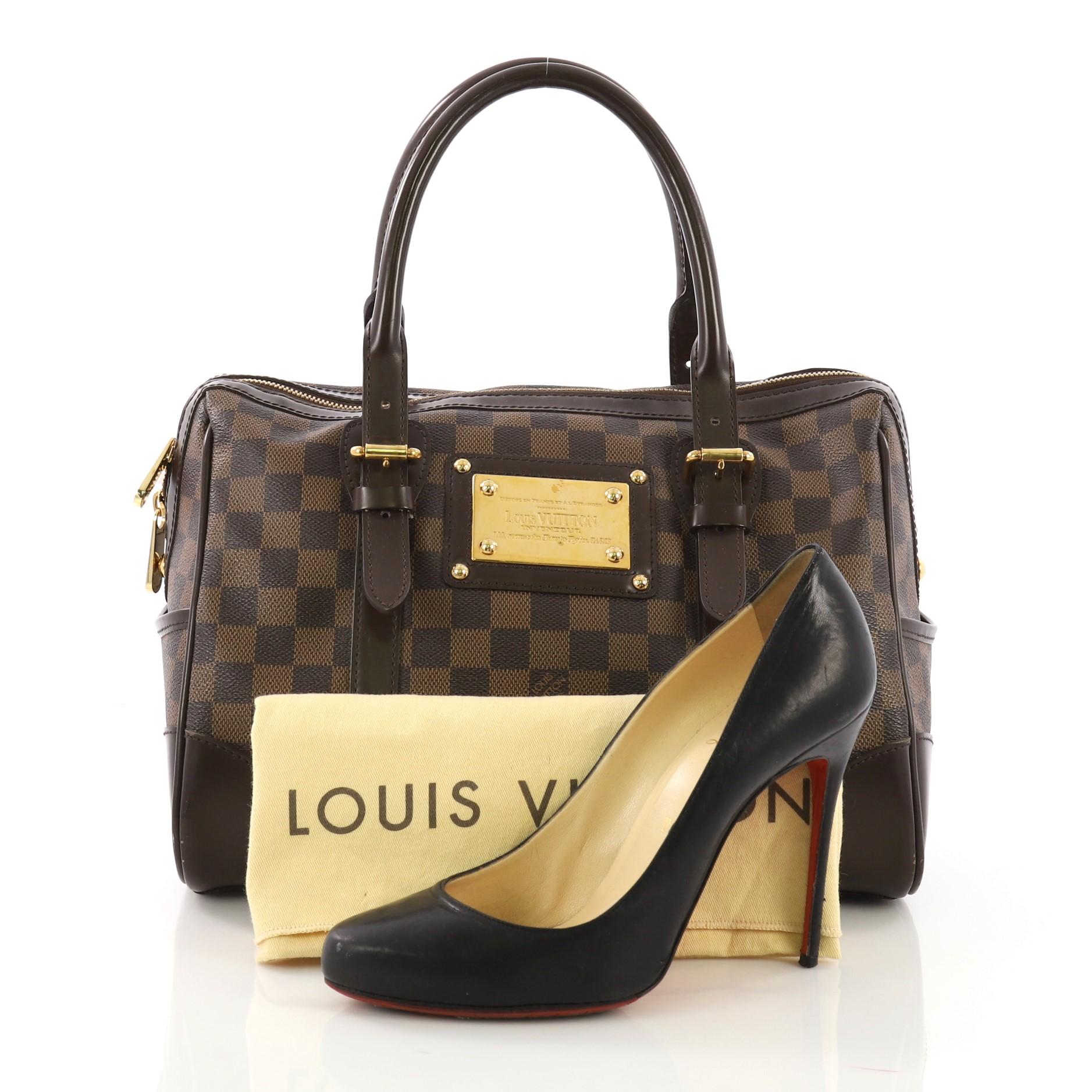 This Louis Vuitton Berkeley Handbag Damier, crafted from damier ebene coated canvas, features dual rolled leather handles with belt and buckle details, exterior side pockets, and gold-tone hardware. Its top zip closure opens to a red microfiber