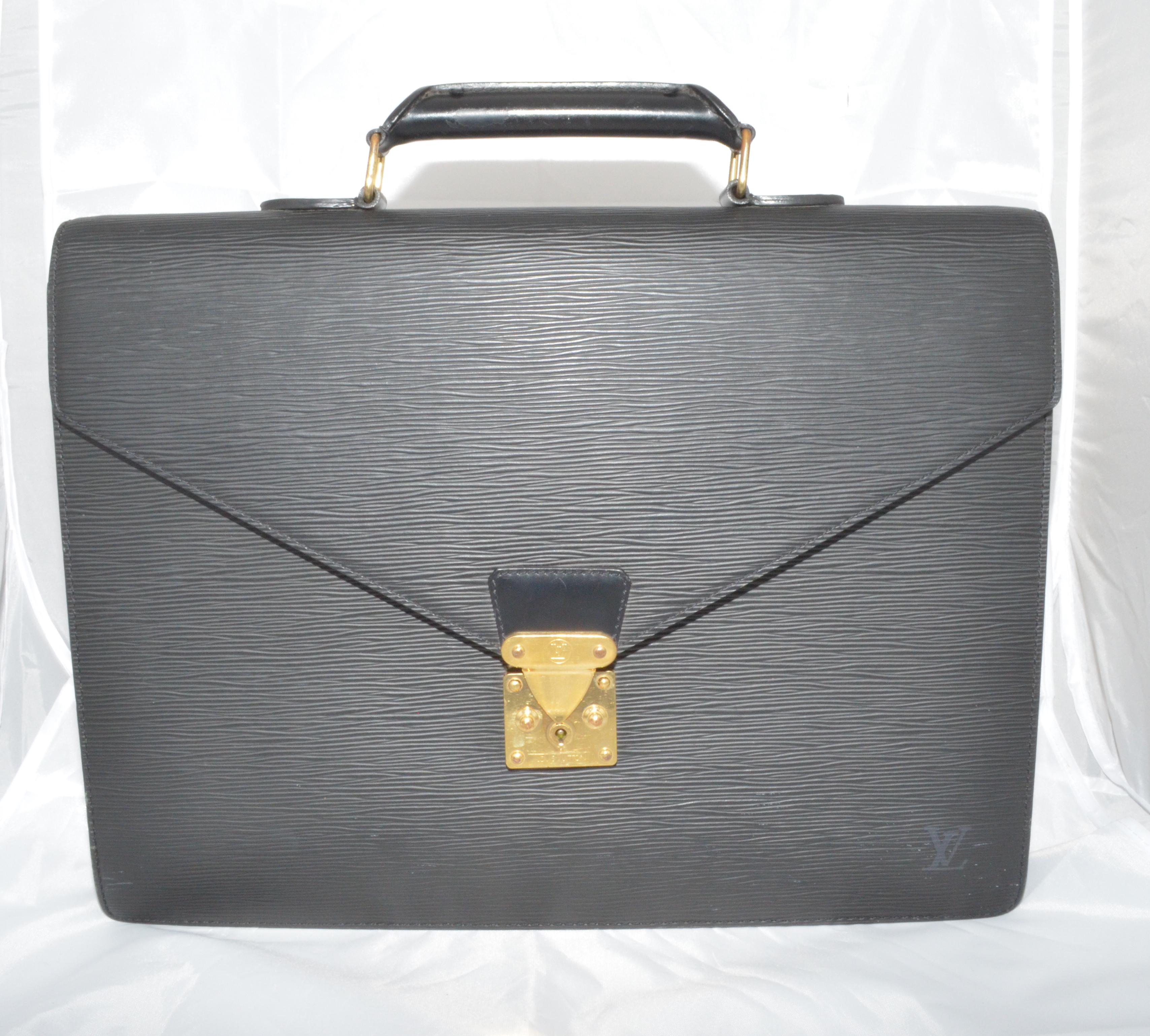 Louis Vuitton Epi leather briefcase is featured in black with gold hardware, a top handle, and an exterior back pocket. Interior is fully lined in leather and has two separated compartments with pockets. Made in France, date code: