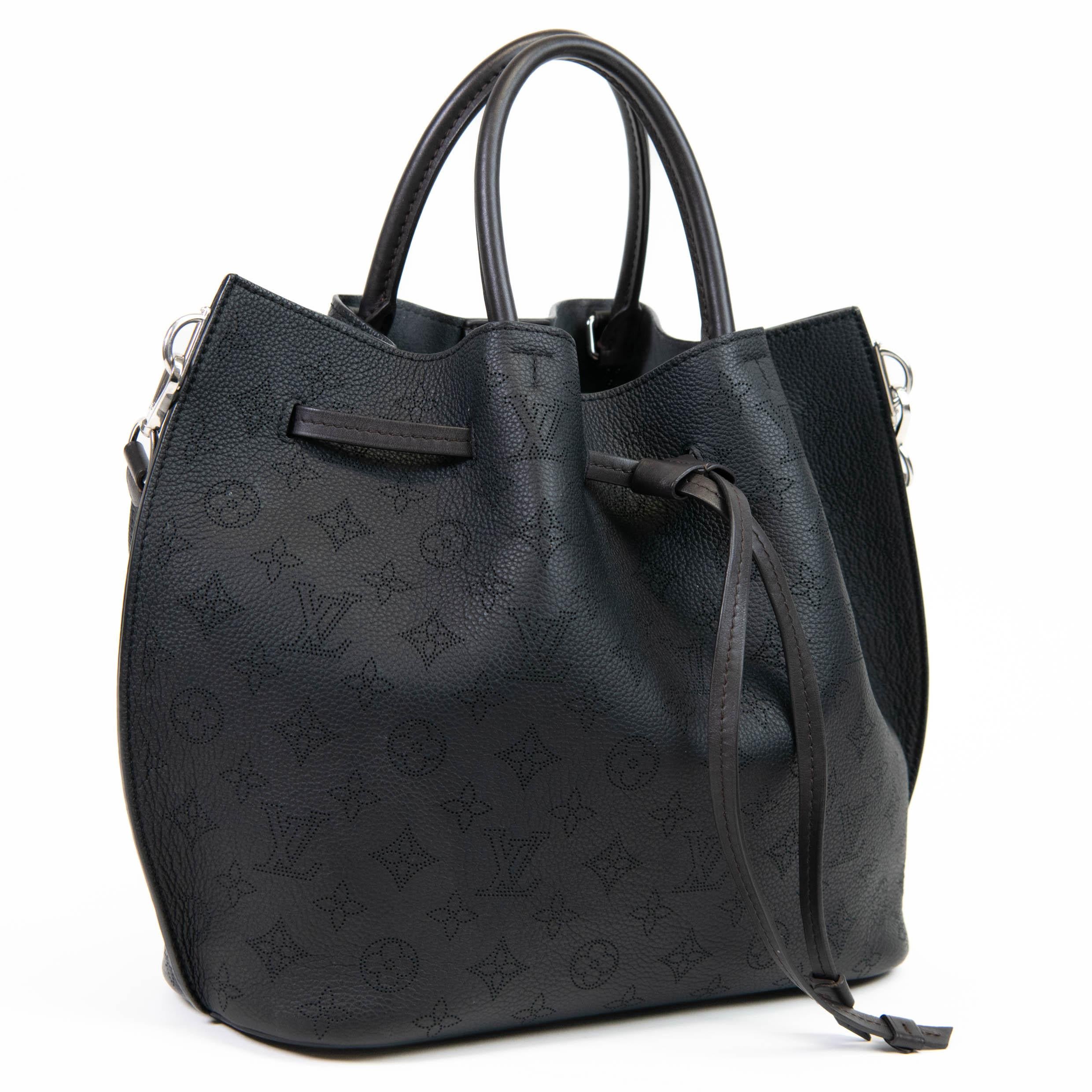 100% Authentic

This chic shoulder bag is crafted of fine mahina leather with perforated monogram detail in black. The shoulder bag features a pull cinch cord, optional shoulder strap, rolled top handles, and polished silver hardware. The top opens