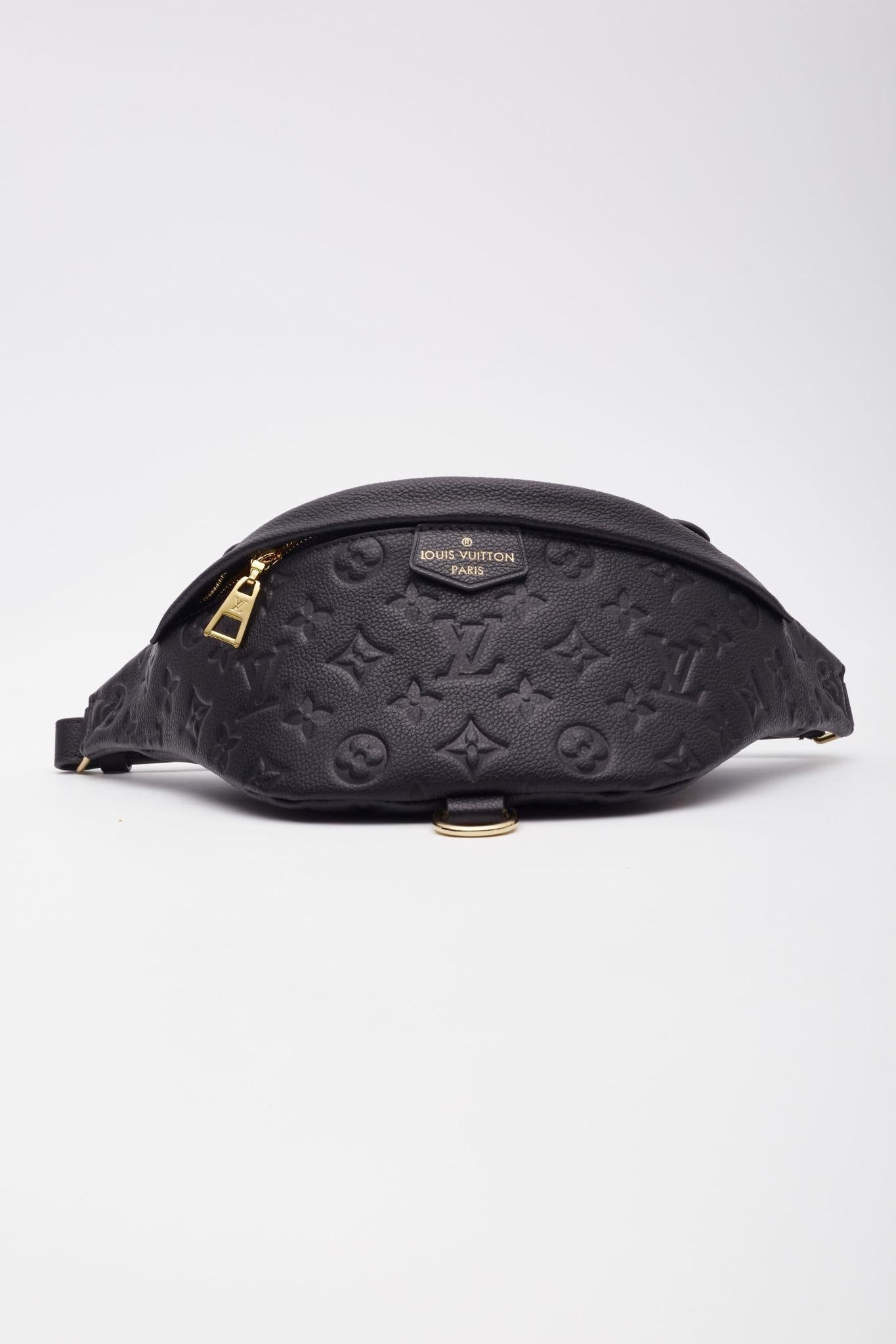 This stylish belt bag is made of traditional Louis Vuitton monogram-embossed calfskin leather in black. The bag features a leather top handle, an adjustable waist strap, and a rear zipper pocket. The main zipper opens to a orange microfiber