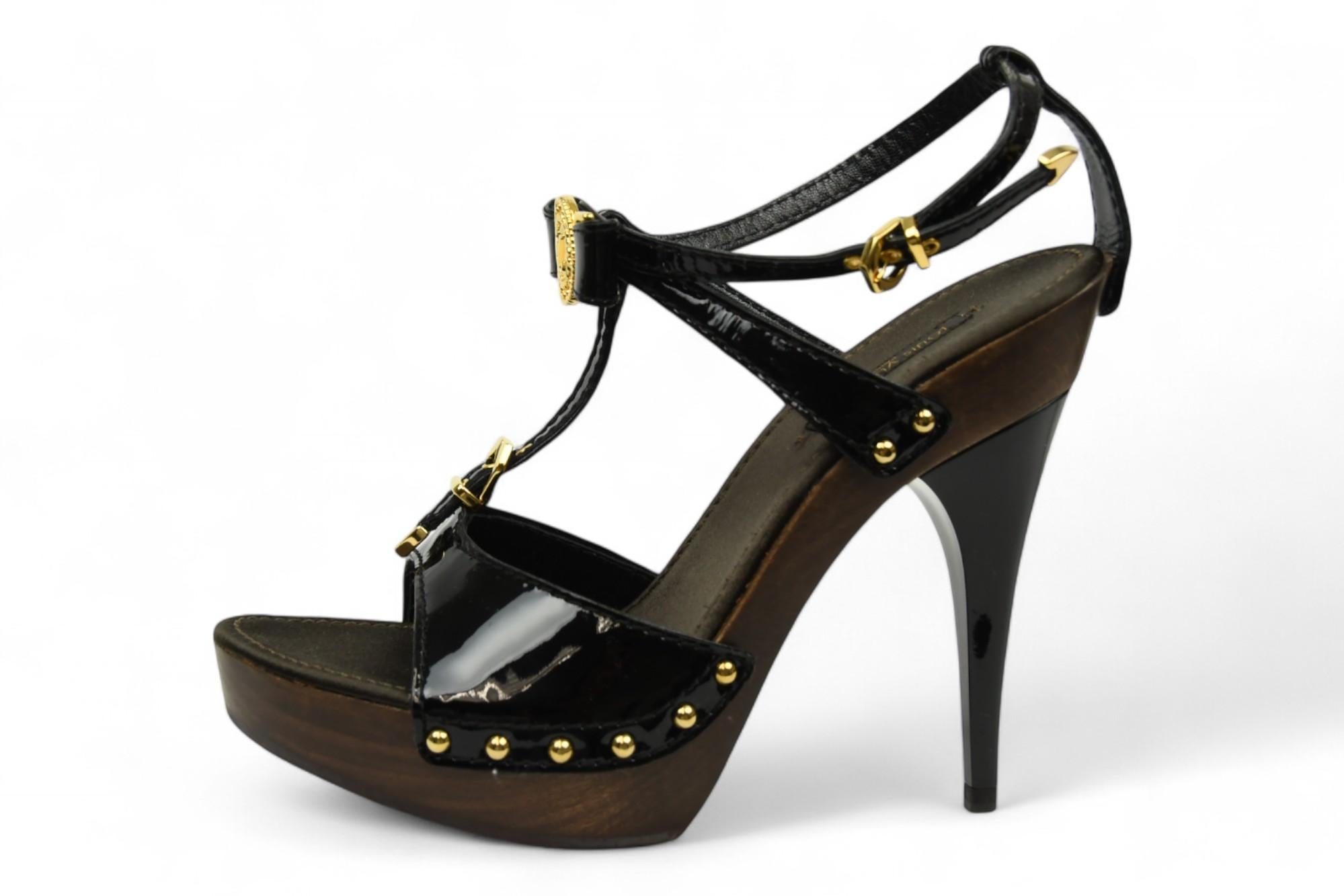 Ces sandales Louis Vuitton exsudent la sophistication high-glam avec une finition audacieuse et sculpturale. Confectionnée en cuir verni noir brillant, cette silhouette à brides est ornée d'accessoires en métal doré, dont les médaillons et les