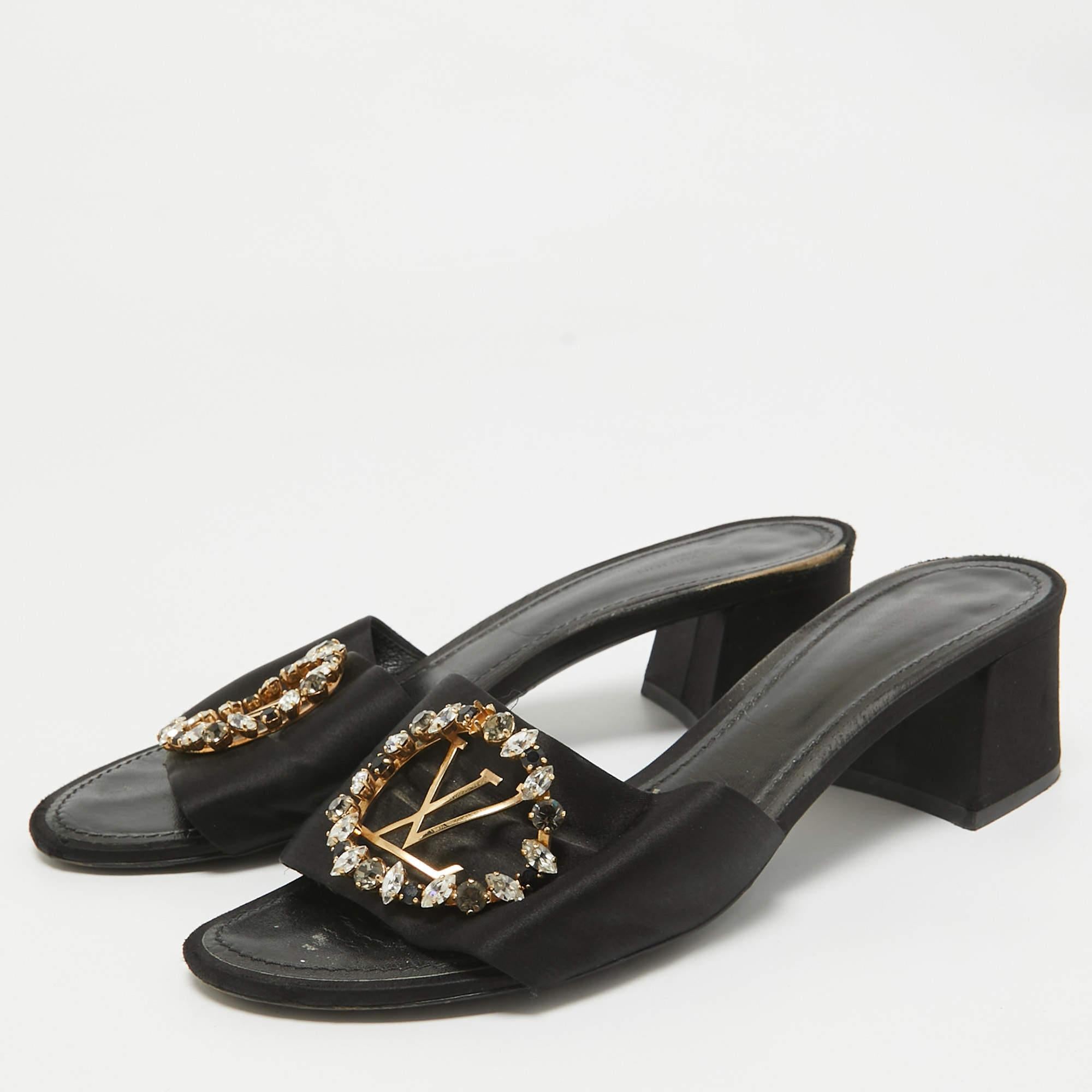 Louis Vuittons Madeleine sandals exude a refined style and sophisticated vibe with their minimal design. Crafted from black satin they feature the LV logo encircled with crystals on the front and open toes. These beauties are finished off with block