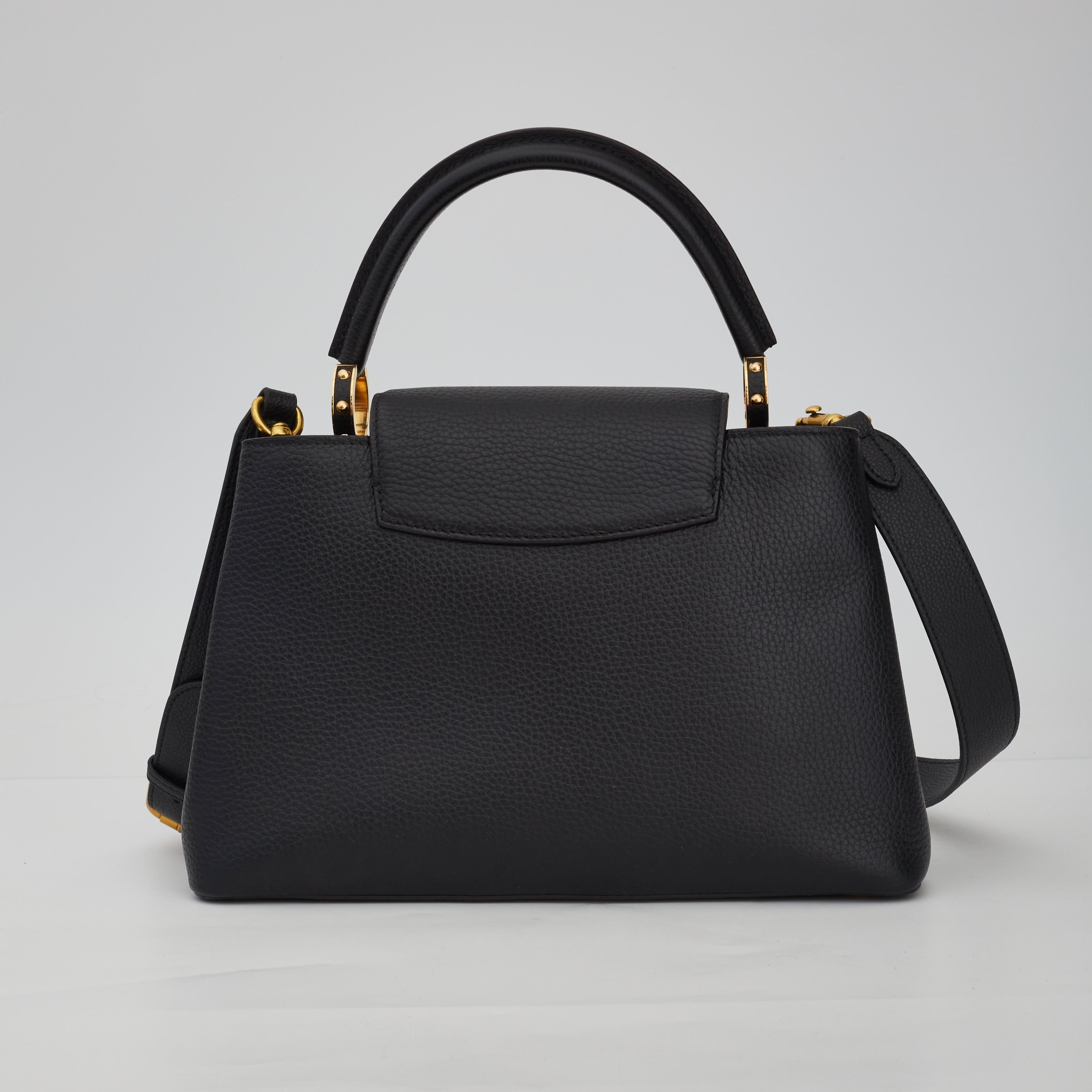 This bag is made of luxurious textured calfskin leather in black. The handbag features a single gold tone hardware, rolled leather reinforced top handle, an optional adjustable shoulder strap, a prominent logo at front face in gold tones and a