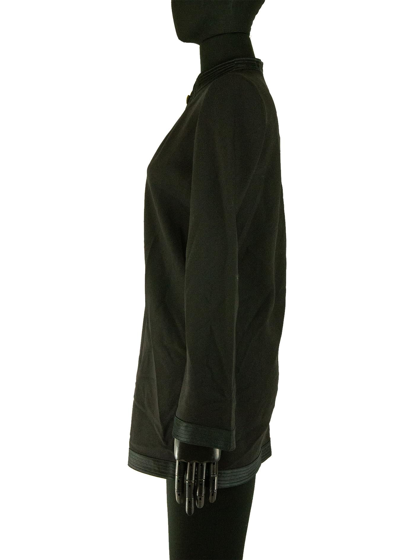 A Louis Vuitton loose-fitting tunic in black wool-based fabric, with satin trimming details. The mandarin satin collar grows into a keep keyhole cut on the neckline, fastened together with a pale yellow flower. This item carries the Louis Vuitton