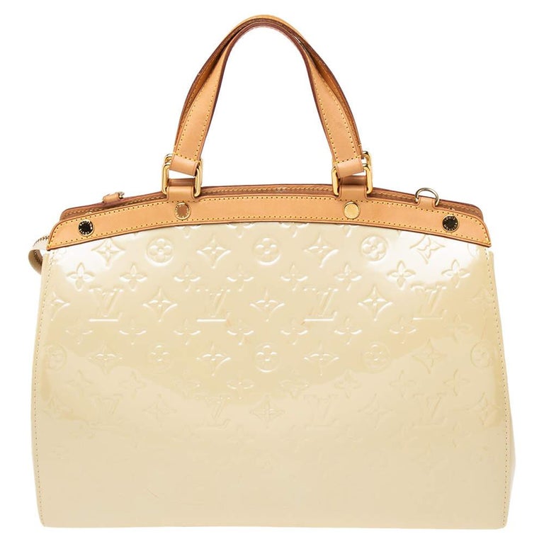 The feminine shape of Louis Vuitton's Brea bag is inspired by the doctor's bag. Crafted from patent leather in cream color, it has a perfectly smooth finish. The fabric interior is spacious to hold your essentials. The bag features double handles,