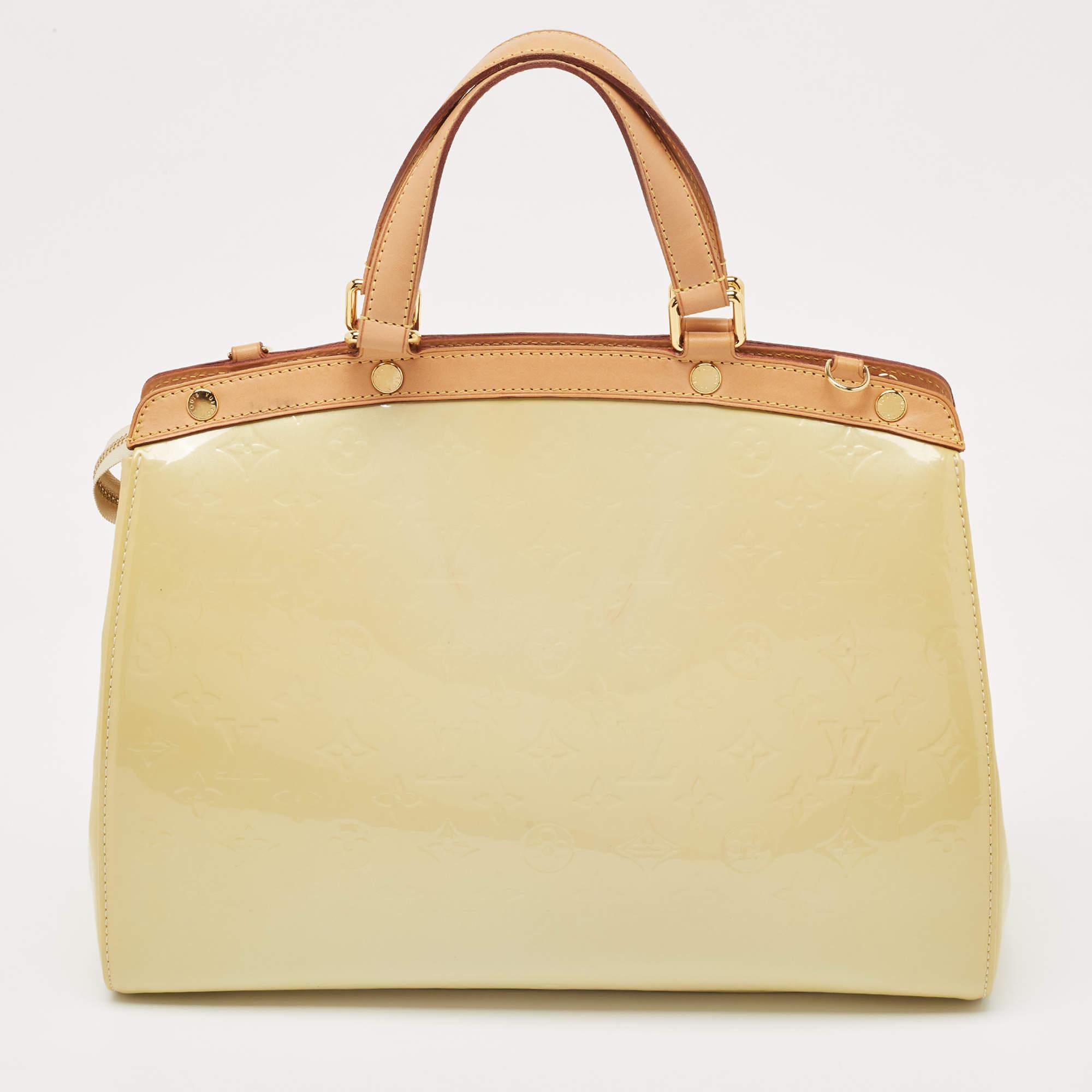 This Brea GM bag from the House of Louis Vuitton will sway you away with its precise shape, style, and design. It is made from Blanc Corail Monogram Vernis into a structured, neat silhouette. It flaunts gold-toned fittings, dual top handles, and a
