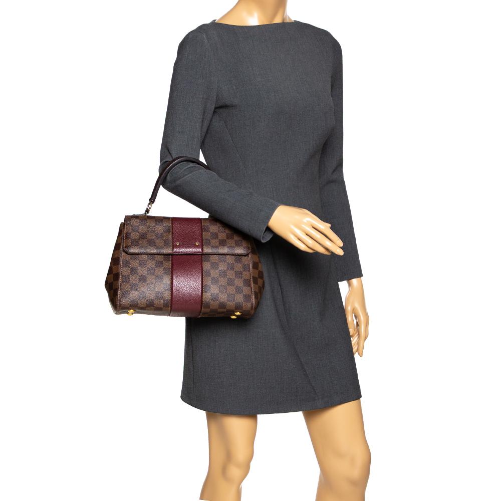 This stylish and chic Bond Street bag by Louis Vuitton comes in a lovely shade of brown. It has been crafted from the brand's signature Damier Ebene canvas and leather. Flawlessly functional, it is the perfect companion for day & night outings. It