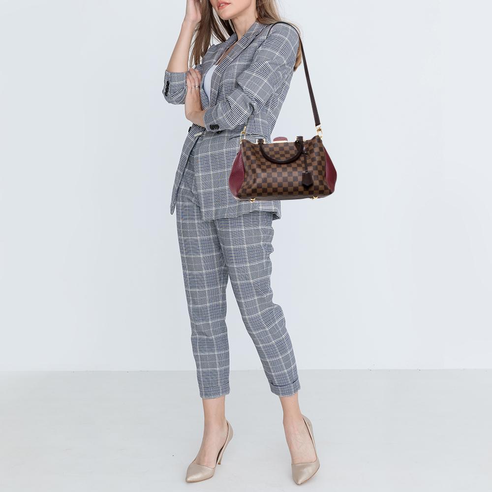 This Brittany BB handbag, from the house of Louis Vuitton, exhibits utility and classic appeal. It is crafted using Damier Ebene canvas and leather. With Alcantara lining and two top handles, this bag will be your indispensable