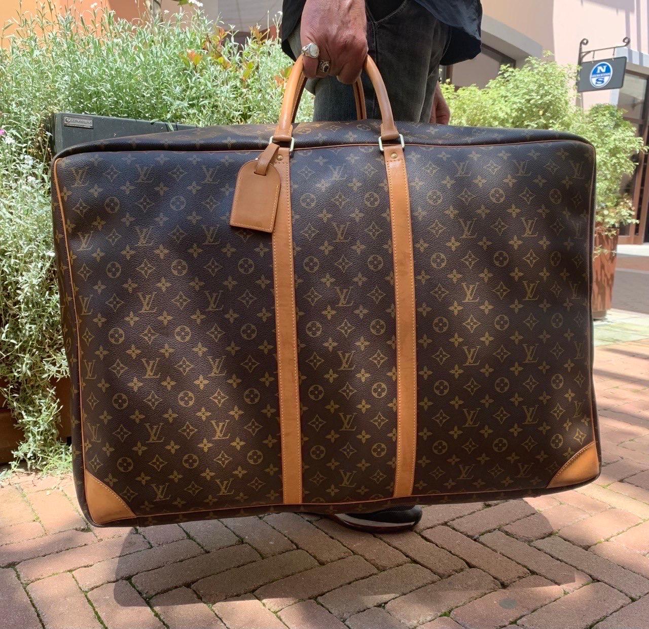 Borsone firmato Louis Vuitton, modello Sirius nella misura 70, realizzato nella classica tela monogram, rifiniture in vacchetta e hardware dorati. Munito di doppio manico in vacchetta per indossare il borsone a mano. Internamente rivestito in tela