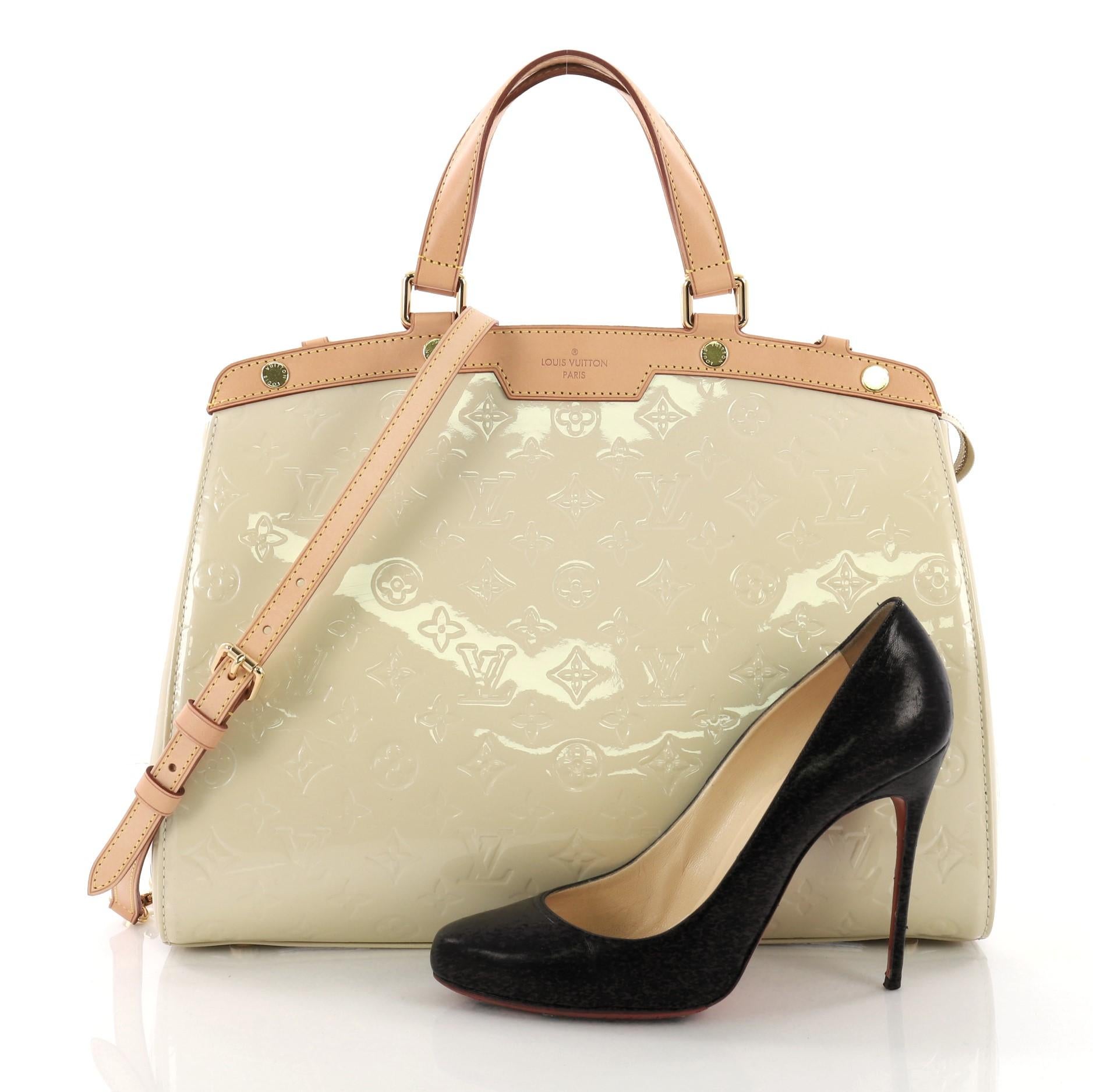 This Louis Vuitton Brea Handbag Monogram Vernis GM, crafted in beige monogram vernis leather with cowhide leather trims, features dual flat handles, protective base studs, and gold-tone hardware. Its top zip closure opens to a beige fabric interior
