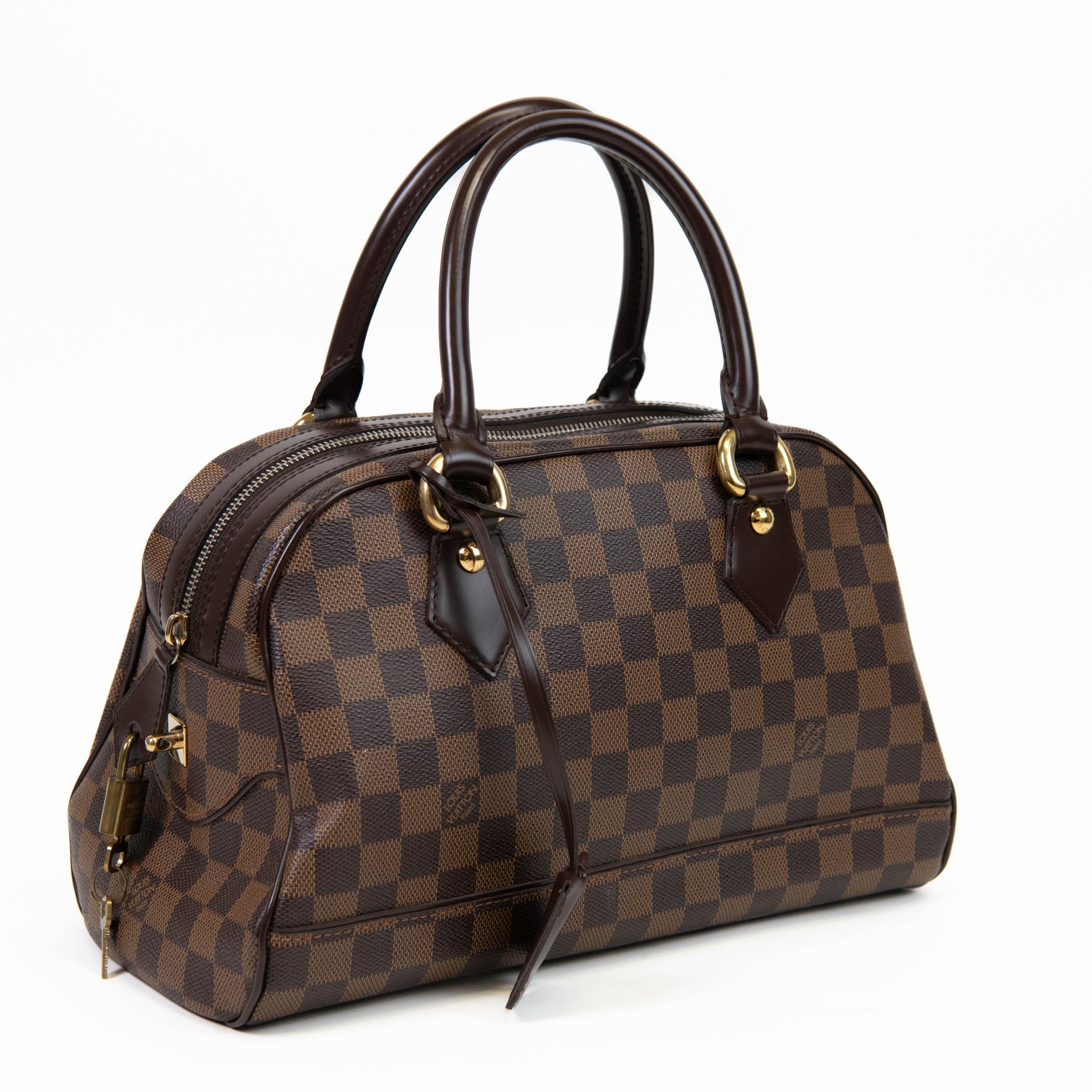 100% Authentic

This stylish tote is crafted of Louis Vuitton's signature Damier check canvas in brown. This bag features dark chocolate brown leather top handles with matching trim and polished gold hardware. The top zipper opens to a scarlet red