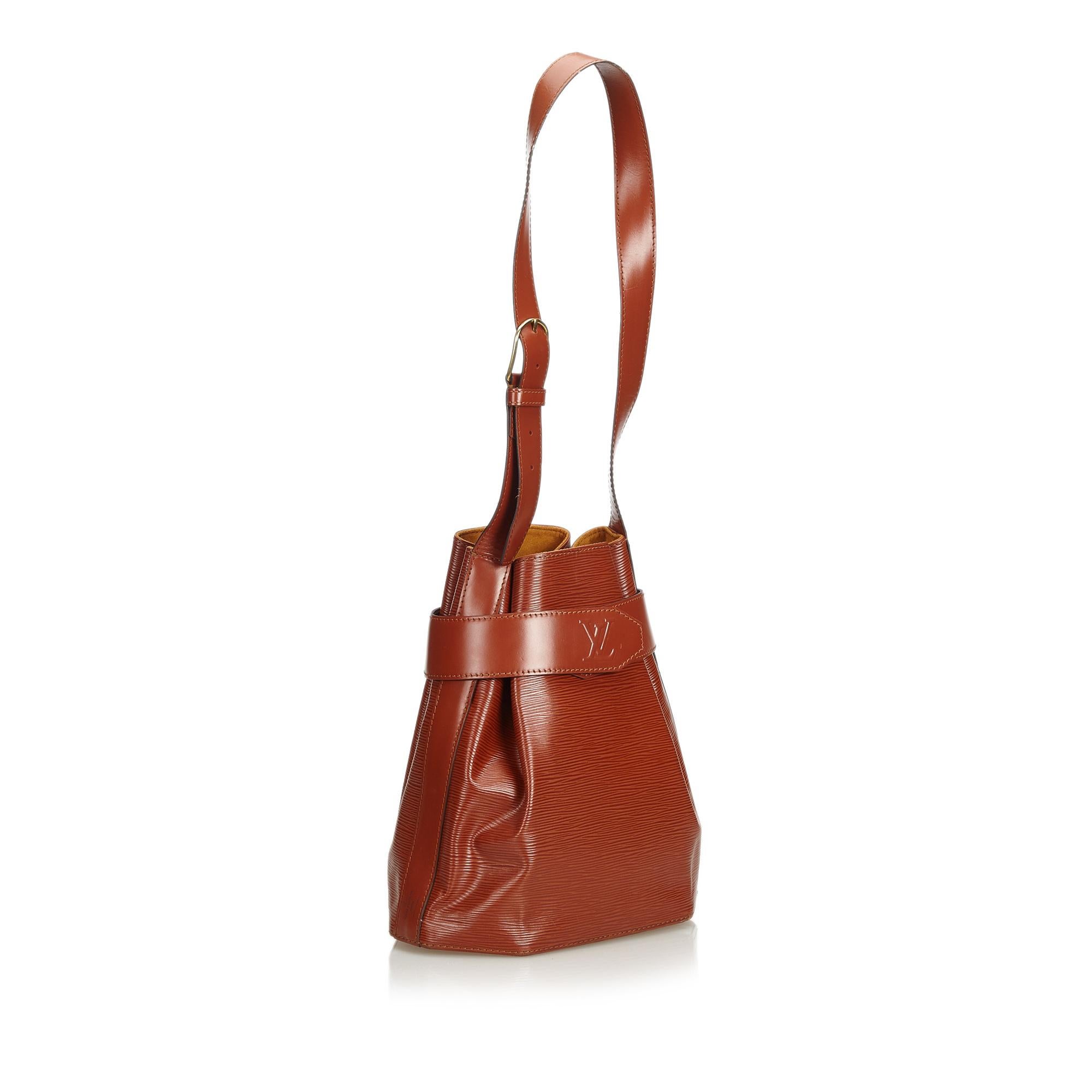 The Sac dEpaule features Epi leather body, an open top with a belt closure secured by a magnetic clasp, an adjustable shoulder strap, and Alcantara lining. It carries as B+ condition rating.

Inclusions: 
This item does not come with