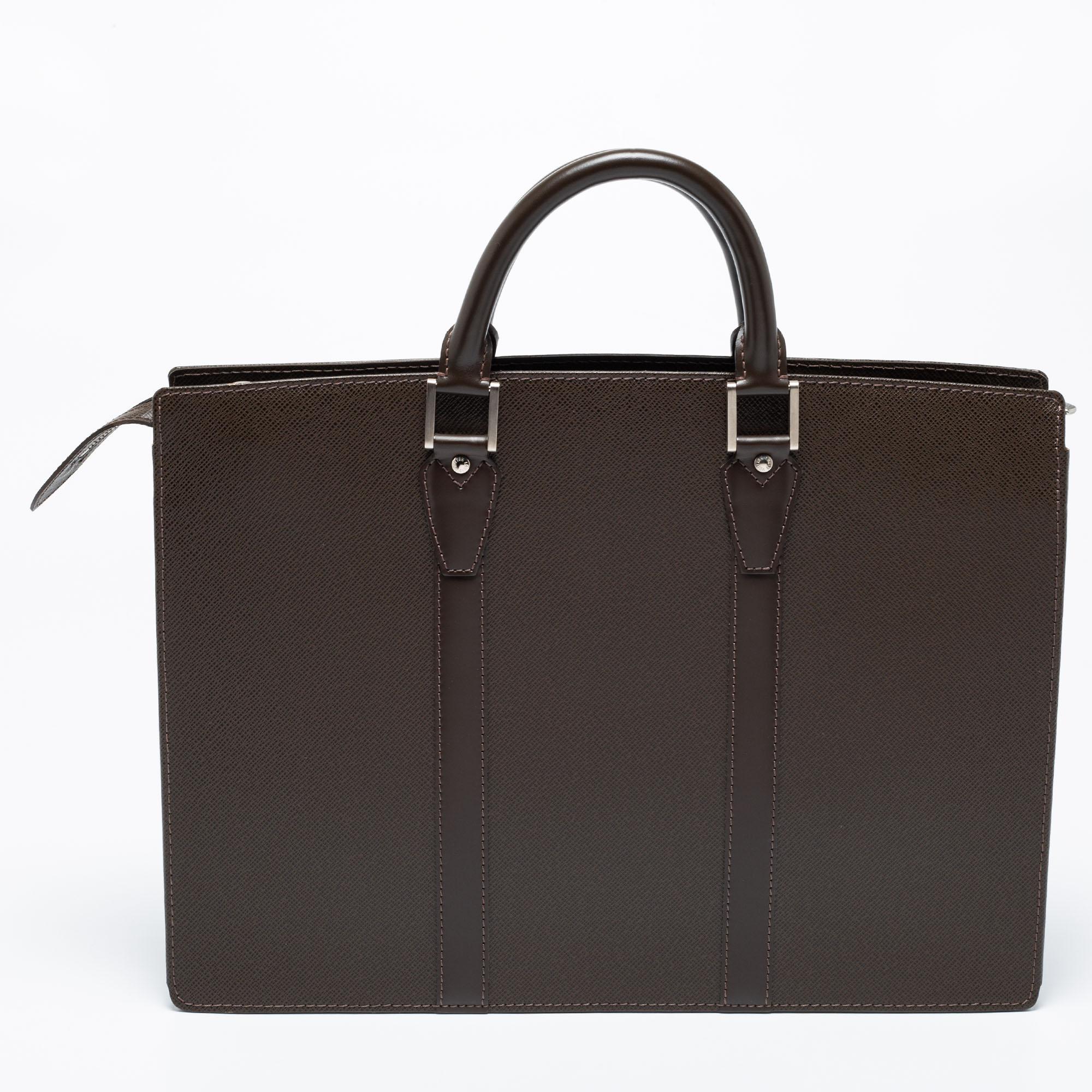 This Louis Vuitton briefcase brings such a grand shape that you're sure to look fashionable whenever you carry it. It has been crafted from brown Taiga leather and is designed with two top handles and canvas compartments where you can carry your