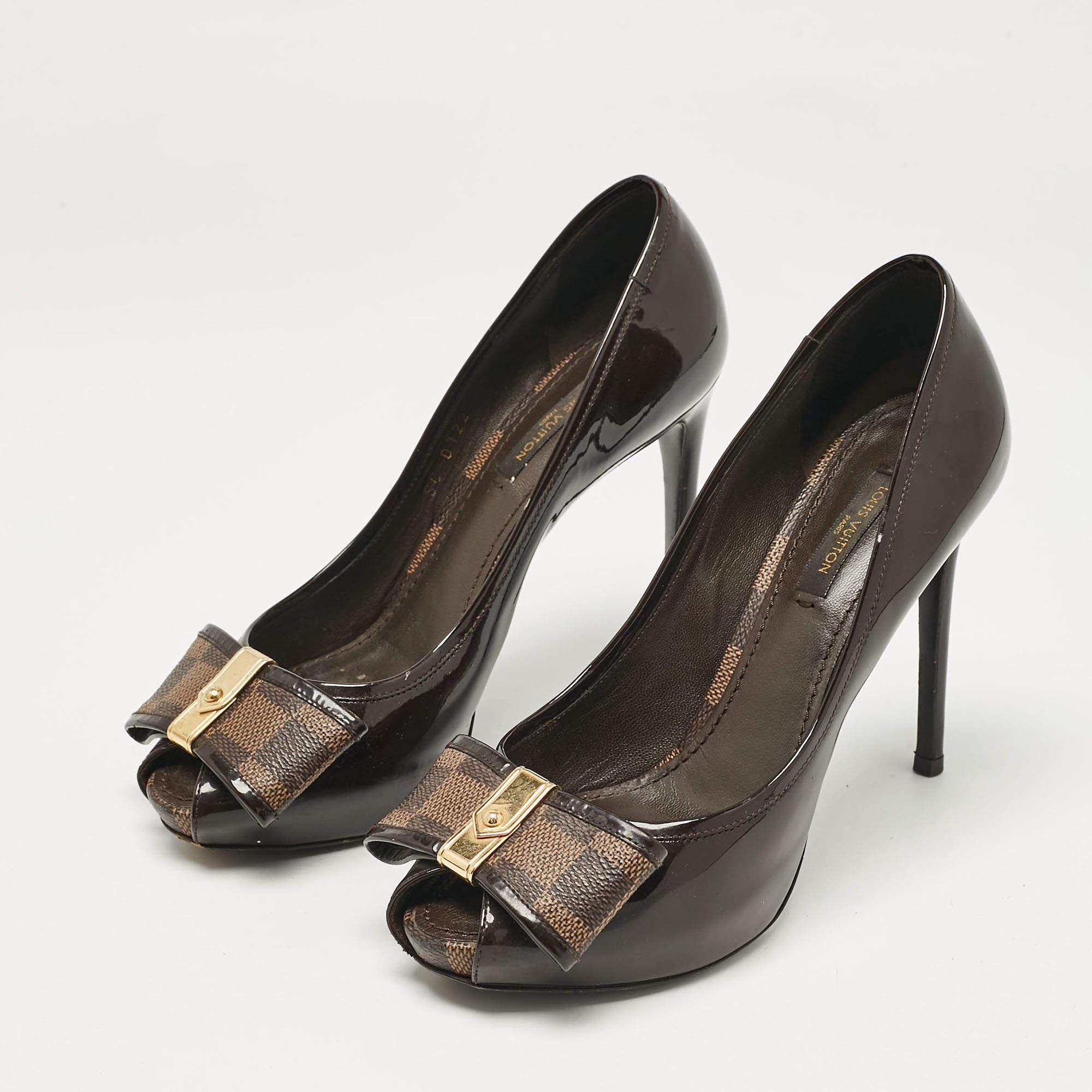 Louis Vuitton caracteriza la clase como nadie. Estos zapatos de salón peep toe de la marca están fabricados en charol de calidad superior con pespuntes tonales. Llevan lazos de cuadros Damier con detalles en tono dorado en los empeines  Tacones de