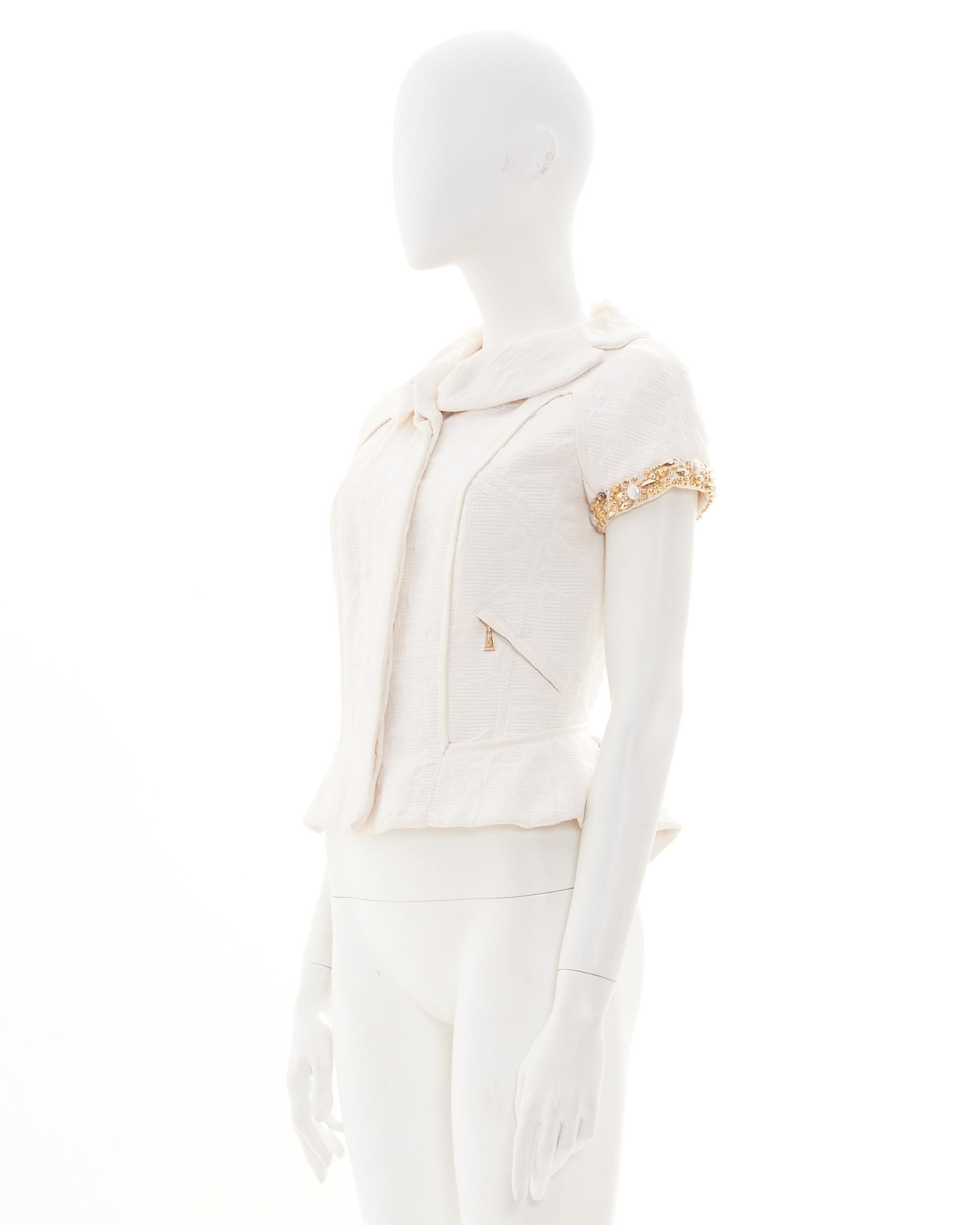 - Diseñado por Marc Jacobs
- Vendido por Skof.Archive
- Colección de principios de la década de 2000
- Chaqueta blanca de manga corta
- Mangas embellecidas con detalles florales dorados
- Dobladillo peplum para una silueta estructurada
- Cuello