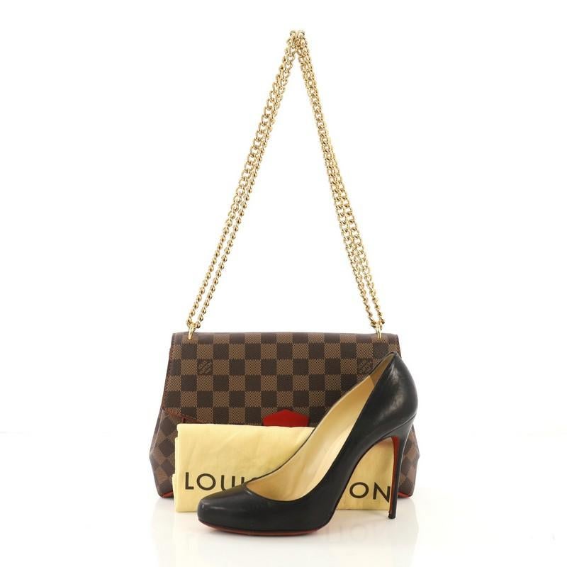 This Louis Vuitton Caissa Clutch Damier, crafted from damier ebene coated canvas, features a chain-link shoulder strap, protective base studs, and gold-tone hardware. Its push-lock closure opens to a red microfiber interior with center zip