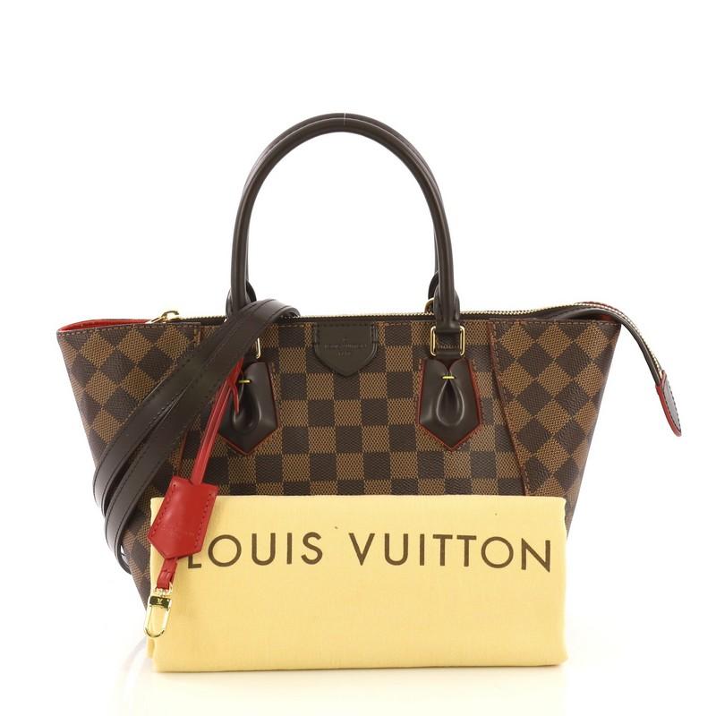 This Louis Vuitton Caissa Tote Damier PM, crafted in damier ebene coated canvas, features dual rolled leather handles, protective base studs, and gold-tone hardware. Its zip closure opens to a red microfiber interior with side slip pockets.