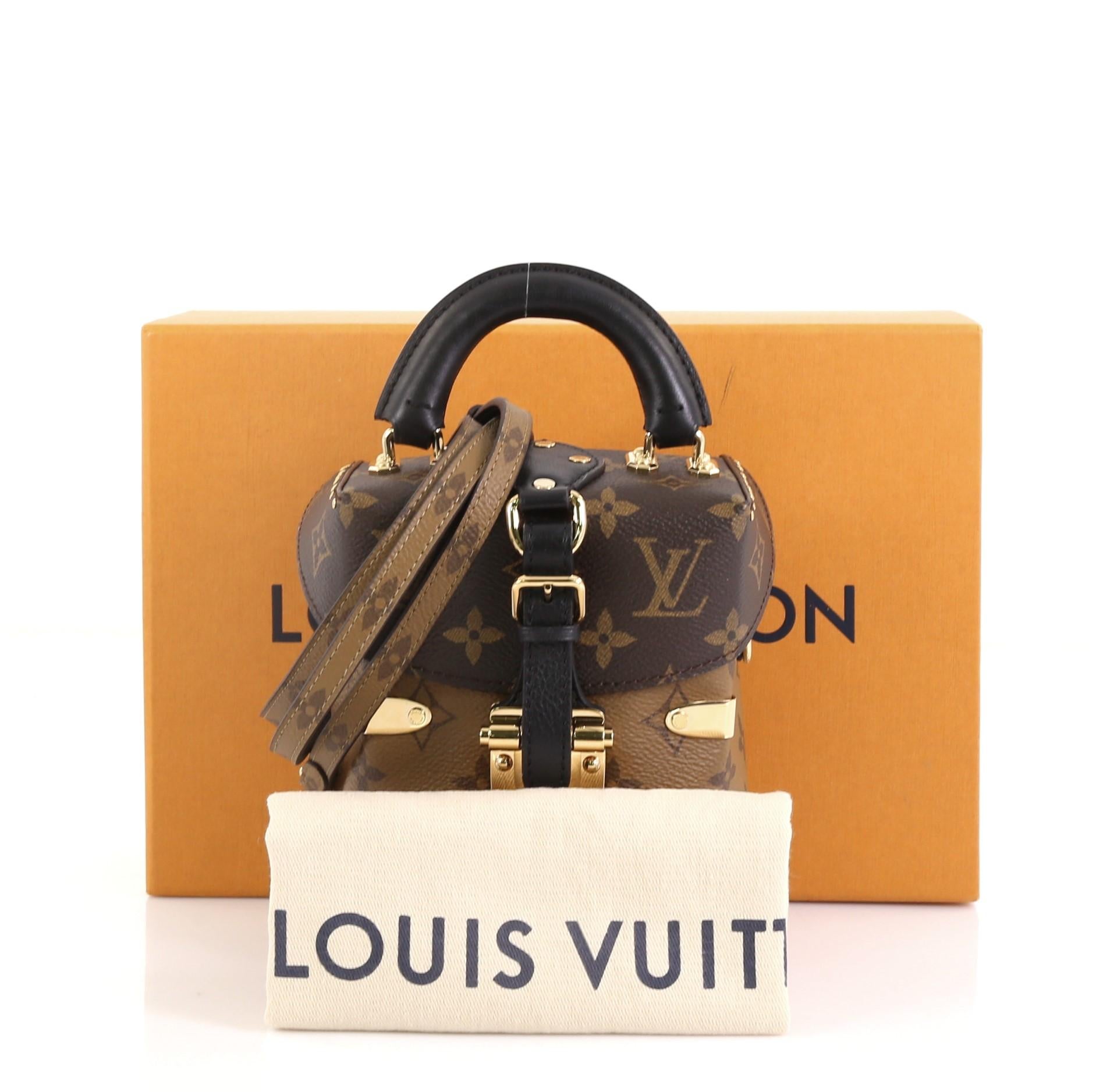 This Louis Vuitton Camera Box Handbag Studded Reverse Monogram Canvas, crafted from brown monogram coated canvas, features leather top handle, stud embellishment, and gold-tone hardware. Its press lock closure opens to a black microfiber interior