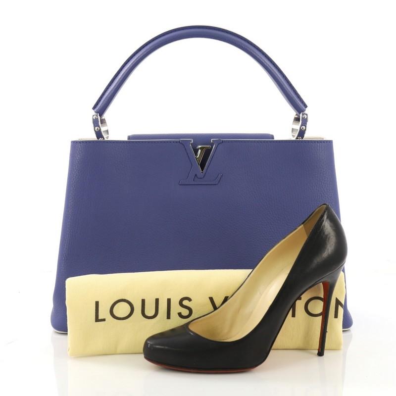 This Louis Vuitton Capucines Handbag Leather MM, crafted in blue leather, features a single loop leather handle secured by jewel-like rings, frontal flap, and silver-tone hardware. Its flap can be tucked inside to reveal the LV logo and opens to a