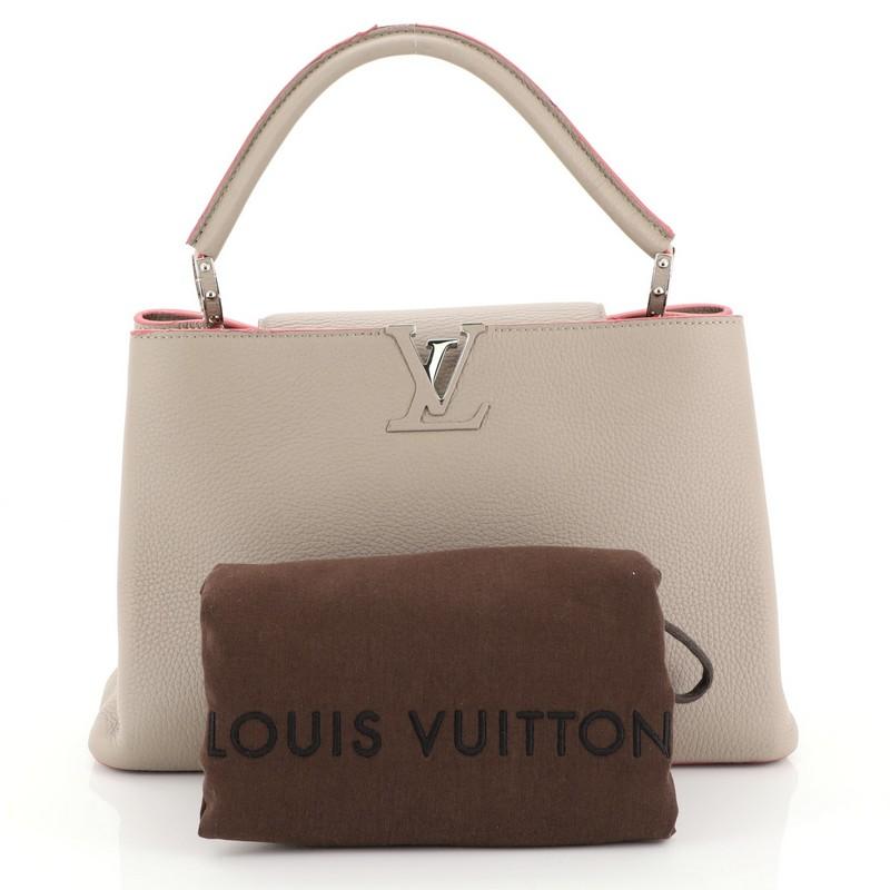 This Louis Vuitton Capucines Handbag Leather MM, crafted in neutral leather, features a single loop leather handle secured by jewel-like rings, frontal flap, and silver-tone hardware. Its flap can be tucked inside to reveal the LV logo and opens to