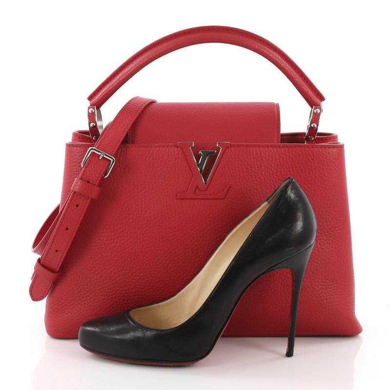 This Louis Vuitton Capucines Handbag Leather PM, crafted from red leather, features a single loop leather handle secured by jewel-like rings, frontal flap with the classic monogram flower hardware, and silver-tone hardware. Its flap can be tucked