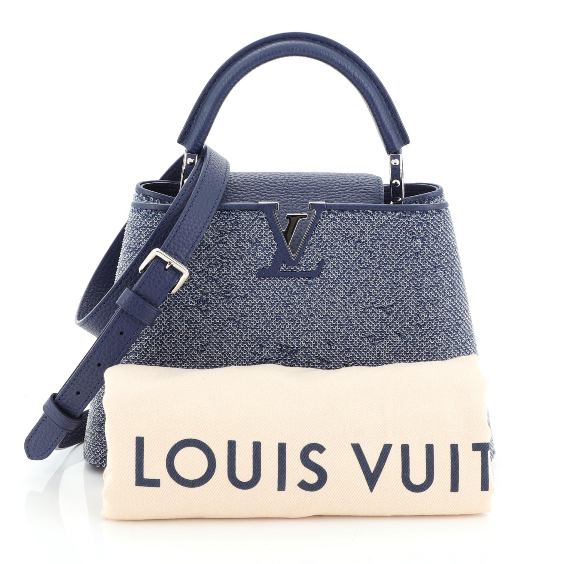 This Louis Vuitton Capucines Handbag Sequins BB, crafted from blue sequins, features a single rolled leather handle secured by jewel-like rings, frontal flap with classic monogram flower, and silver-tone hardware. It opens to a blue leather interior