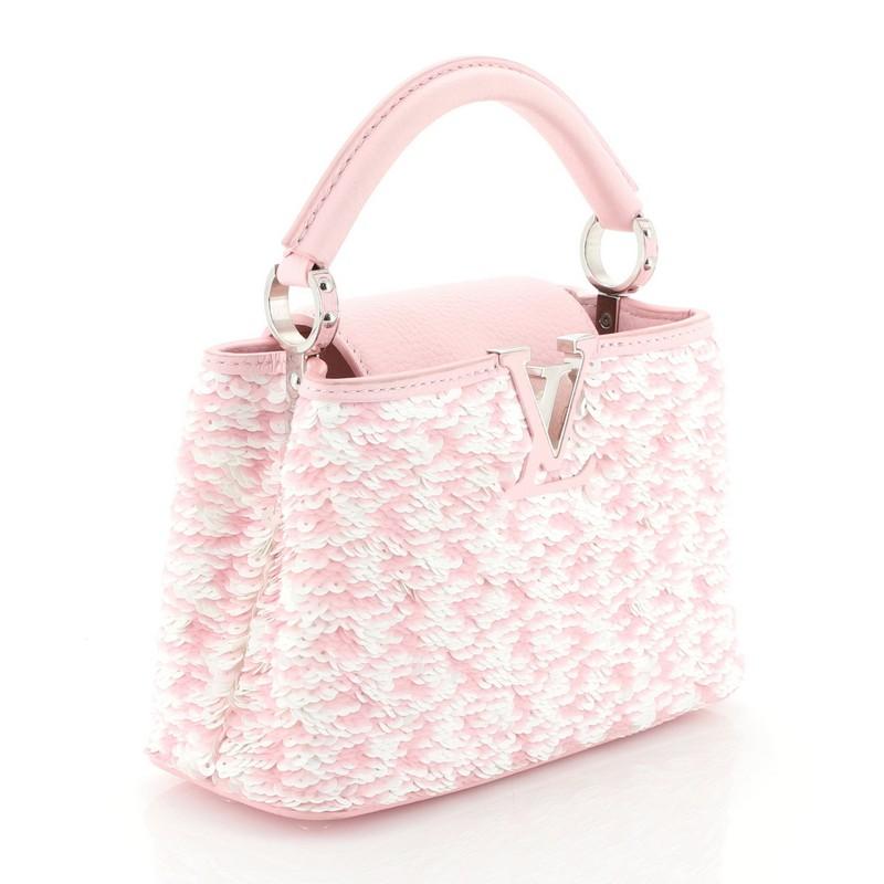 This Louis Vuitton Capucines Handbag Sequins Mini, crafted from white and pink sequins, features a single rolled leather handle secured by jewel-like rings, frontal flap with classic monogram flower, and silver-tone hardware. It opens to a white