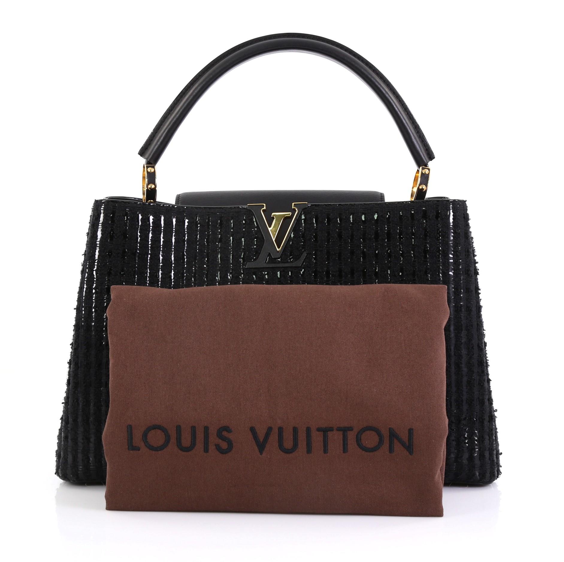 This Louis Vuitton Capucines Handbag Tweed MM, crafted in black tweed and leather, features a single loop leather handle secured by jewel-like rings, frontal flap, and gold-tone hardware. Its flap can be tucked inside to reveal the LV logo and opens