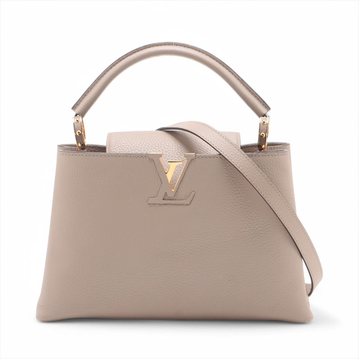 The Louis Vuitton Capucines MM in Galet is an elegant handbag crafted from full-grain Taurillon leather in a sophisticated beige hue. The bag features a distinctive flap that can be worn two ways: outside to reveal a Monogram Flower or inside to