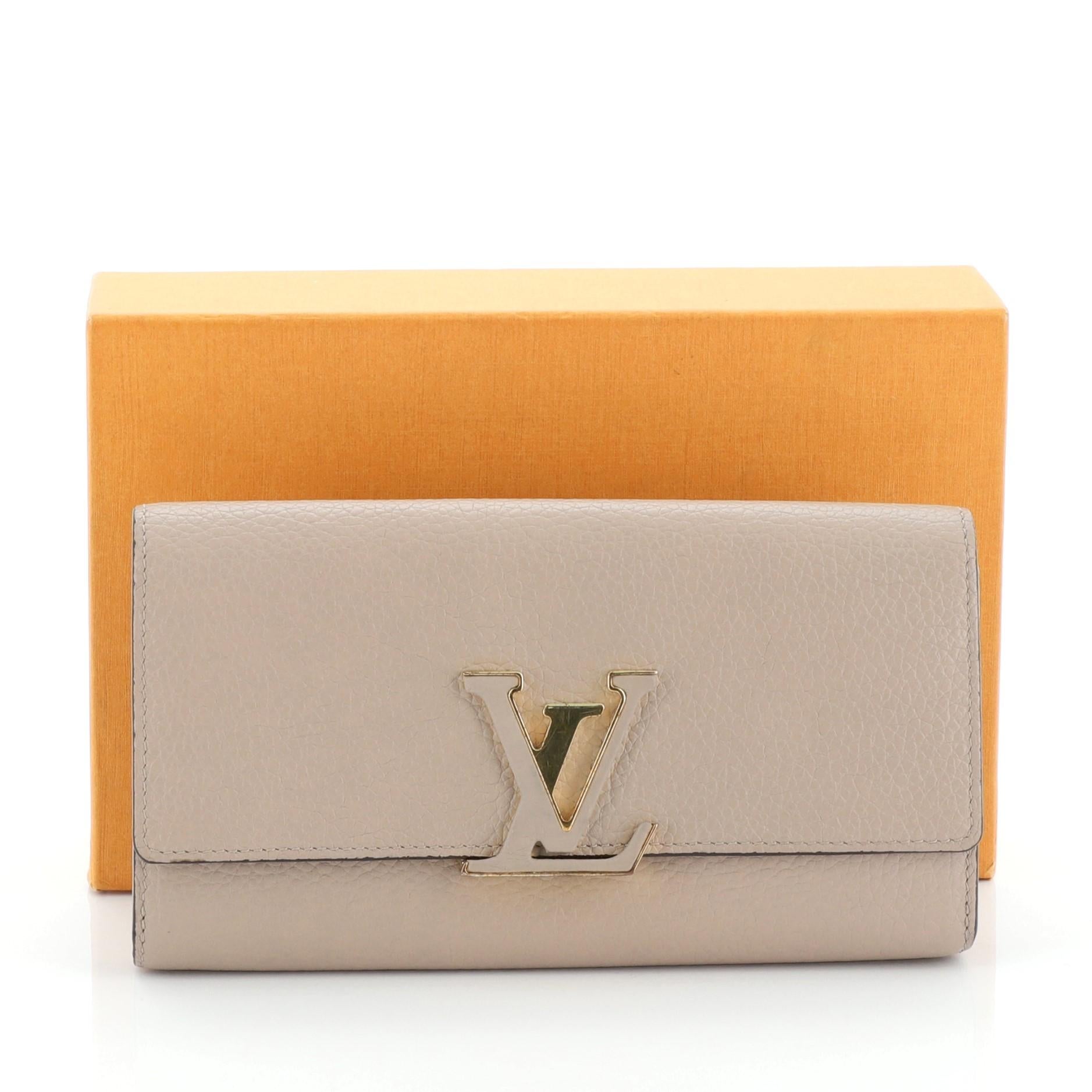 This Louis Vuitton Capucines Wallet Leather, crafted in neutral leather, features a signature LV logo in front and gold-tone hardware. Its snap closure opens to a brown leather interior with multiple card slots and middle zip compartment.
